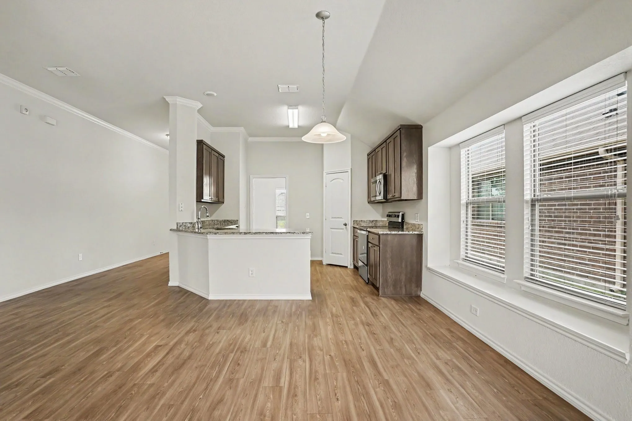 Open-concept living area with wood-finish flooring, crown molding, and a kitchen featuring dark wood cabinetry and stone countertops