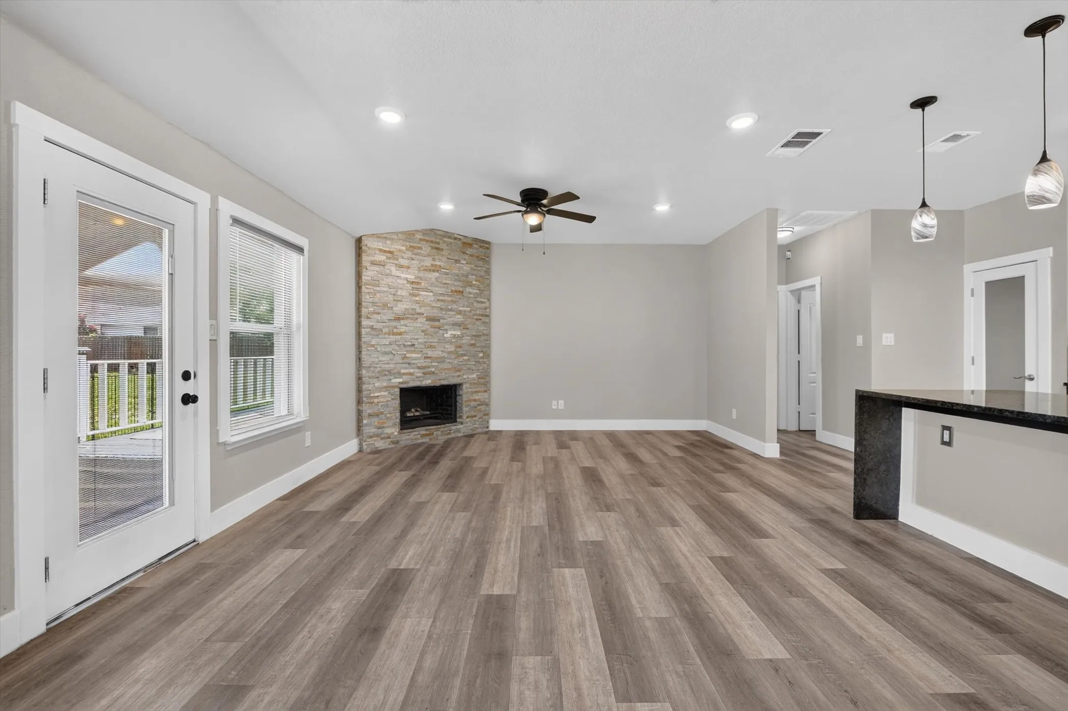 Spacious living area featuring wood-finish flooring, recessed lighting, and a corner fireplace with a stacked stone facade