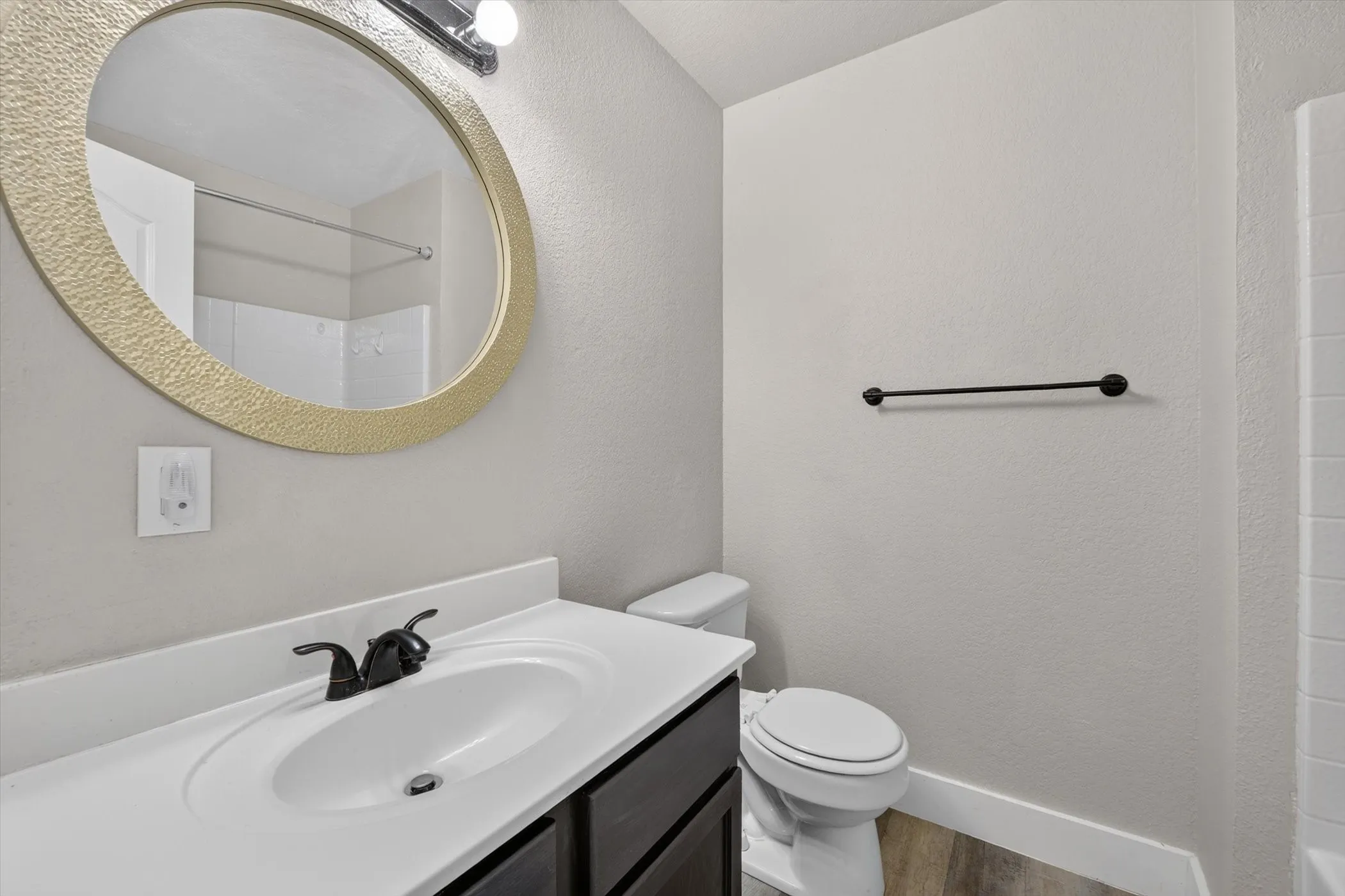 Bathroom featuring a dark wood-finish vanity with an integrated white sink, a matte black faucet, and a large oval mirror with a textured gold-tone frame