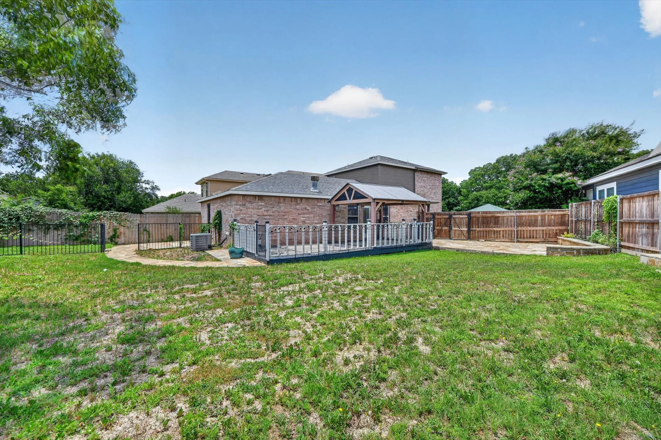 Expansive backyard featuring a large wood-finish deck with white railings, a covered patio area, and a paved stone section