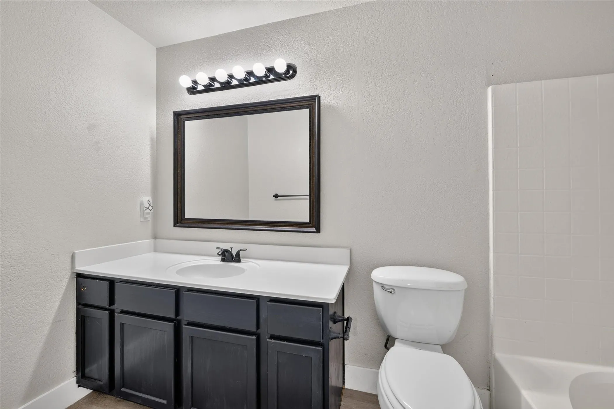 Bathroom featuring a dark wood-finish vanity with a white countertop and integrated sink, framed mirror, and a five-bulb vanity light fixture