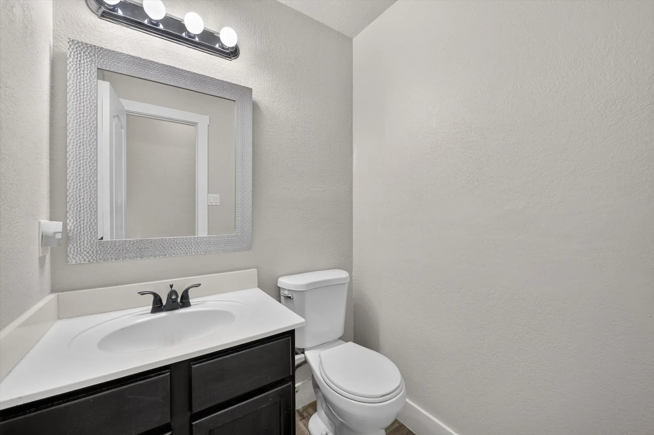 Bathroom featuring a dark wood-finish vanity with a white countertop and integrated sink, a rectangular mirror with a textured frame, and a four-light fixture