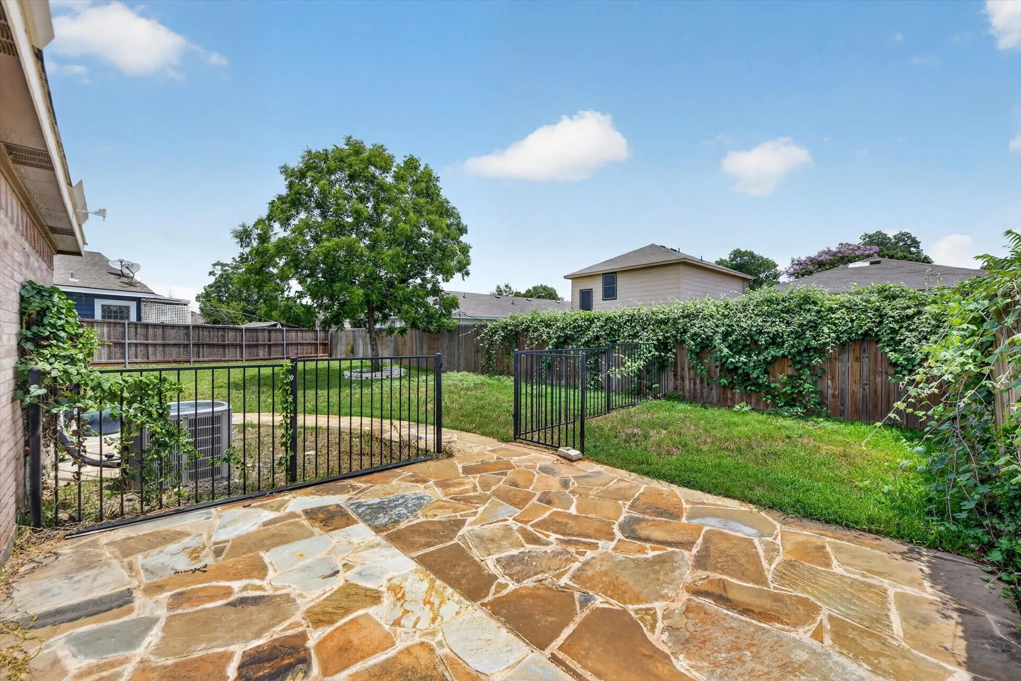 Expansive flagstone patio area with a black metal fence and gate