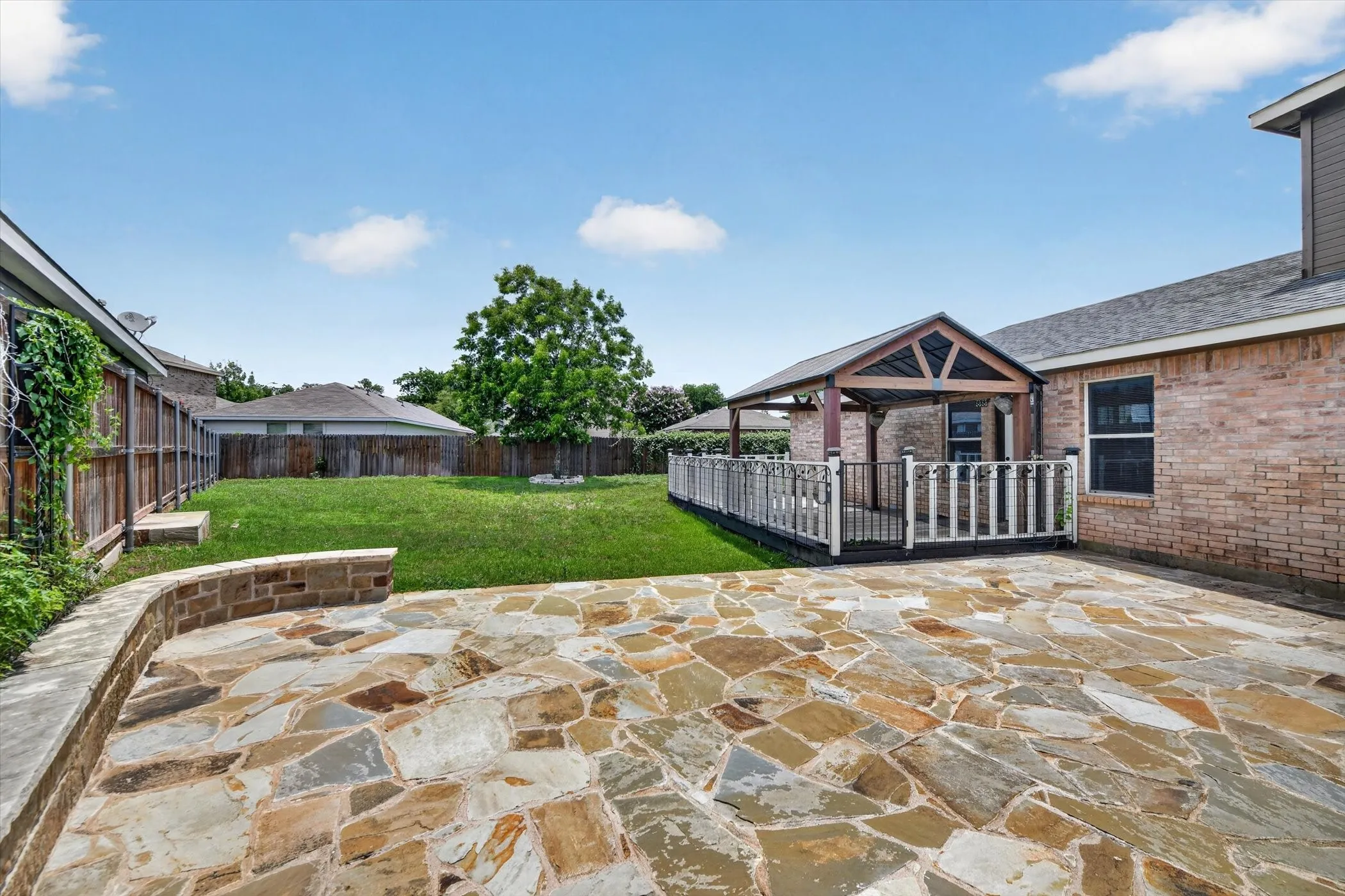 Expansive backyard featuring a natural stone patio, a covered deck with decorative railing, and a sizable lawn area