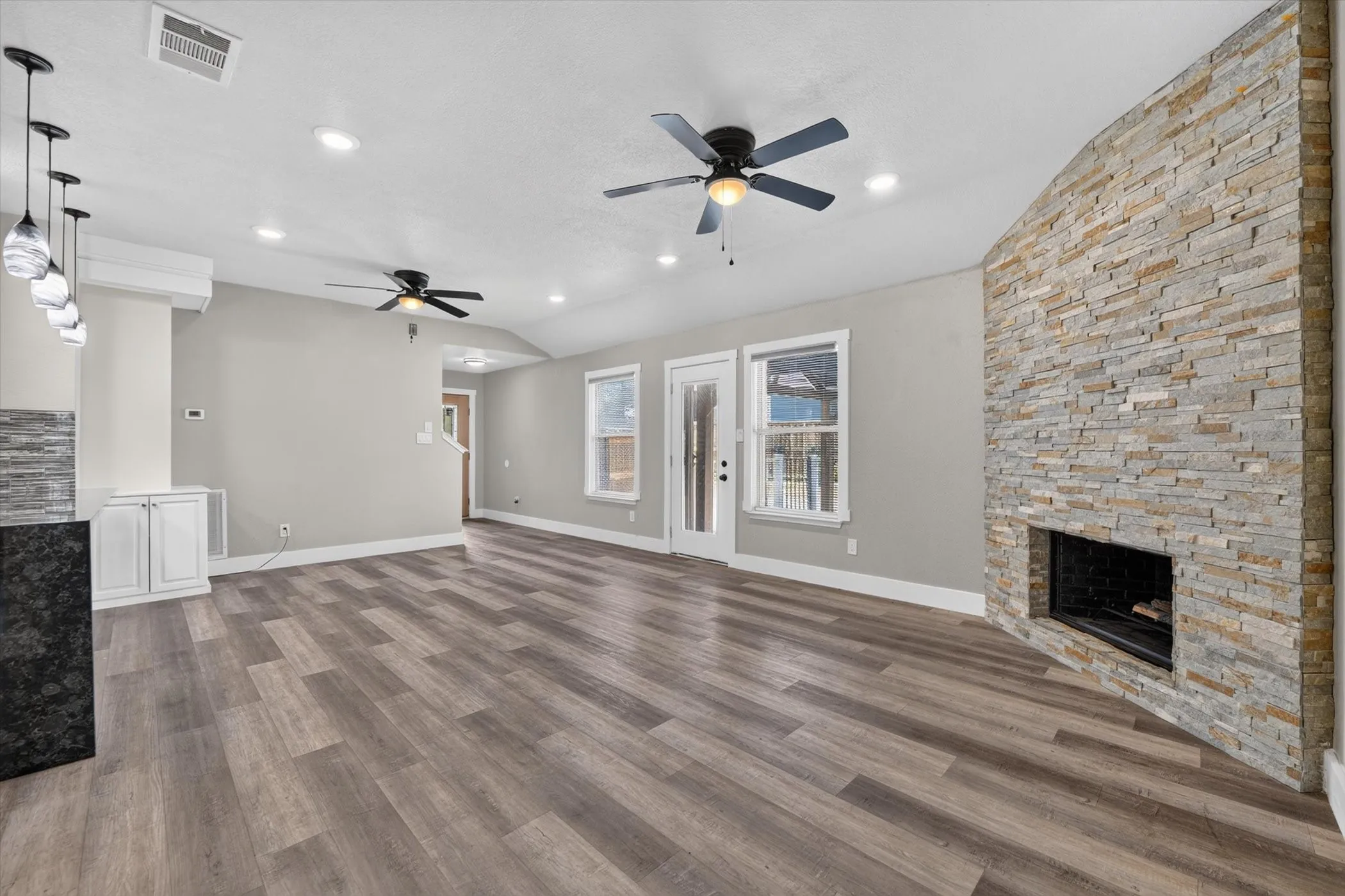 Open-concept living area featuring wood-finish flooring, a stone-clad fireplace, recessed lighting, and dual ceiling fans