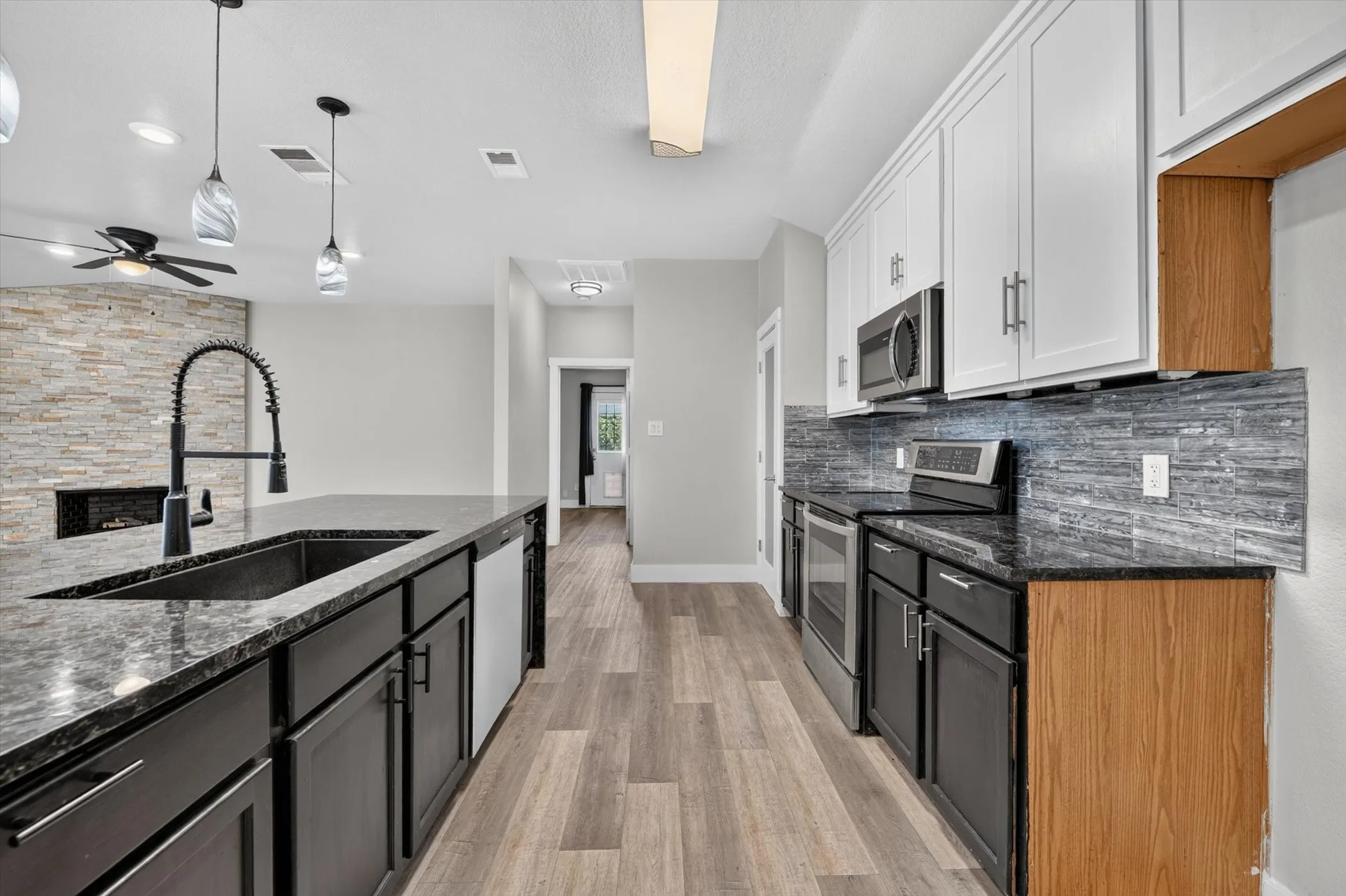 Contemporary kitchen featuring dark cabinetry on the island, white upper cabinetry, and a dark stone countertop