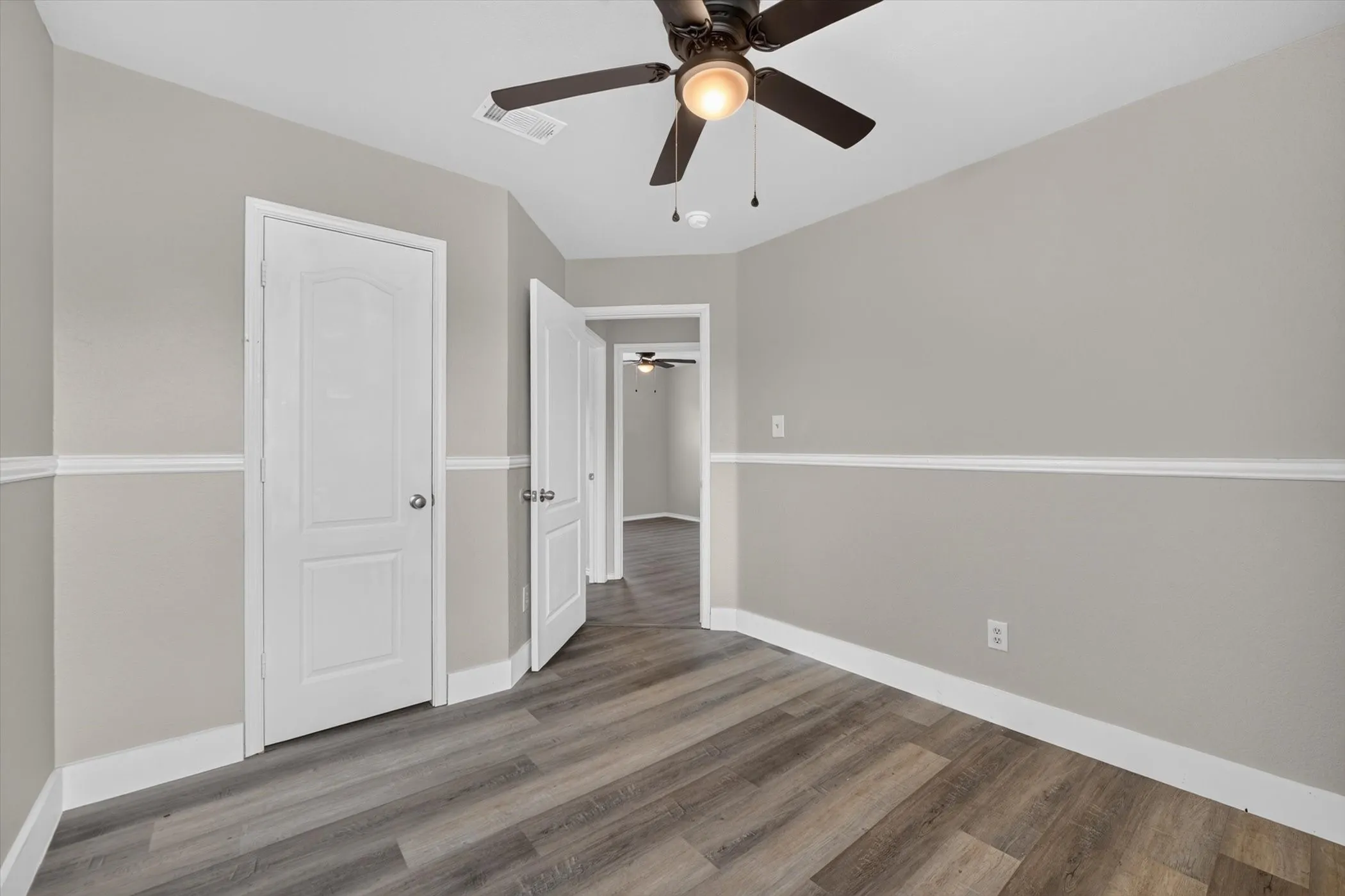 Room featuring wood-finish flooring, light gray walls with white chair rail molding, and a ceiling fan with integrated lighting