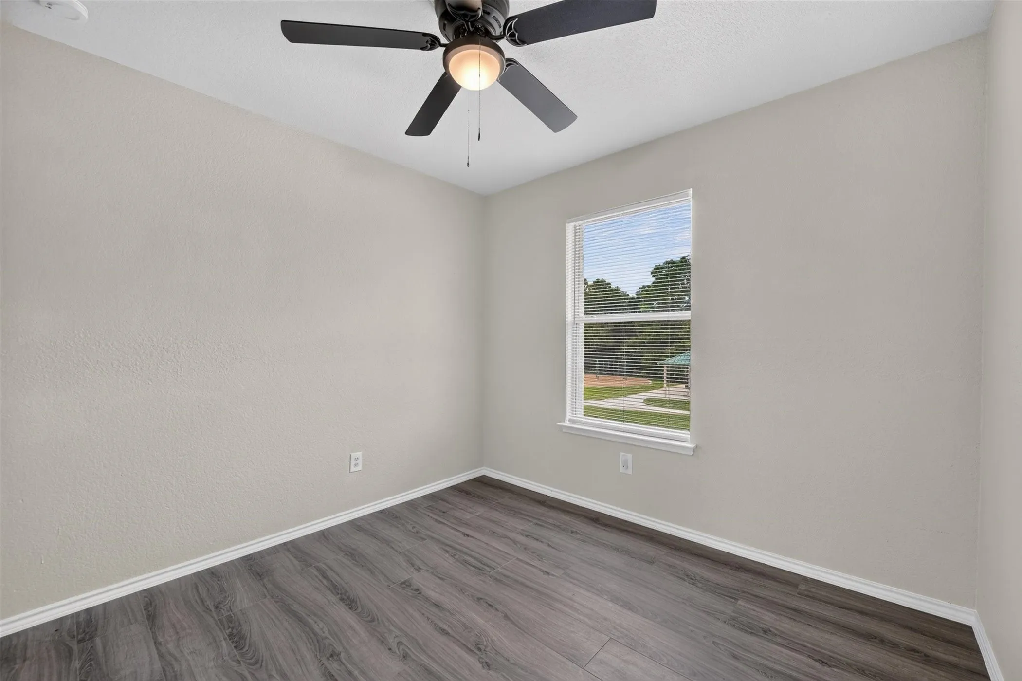 Room featuring wood-finish flooring, a ceiling fan with integrated lighting, and a window with horizontal blinds