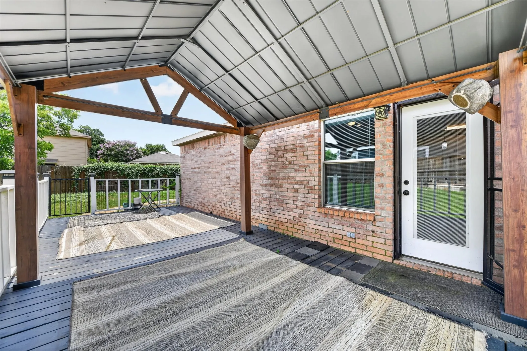 Covered outdoor living area featuring a vaulted metal roof, exposed wood beams, and a wood-finish deck