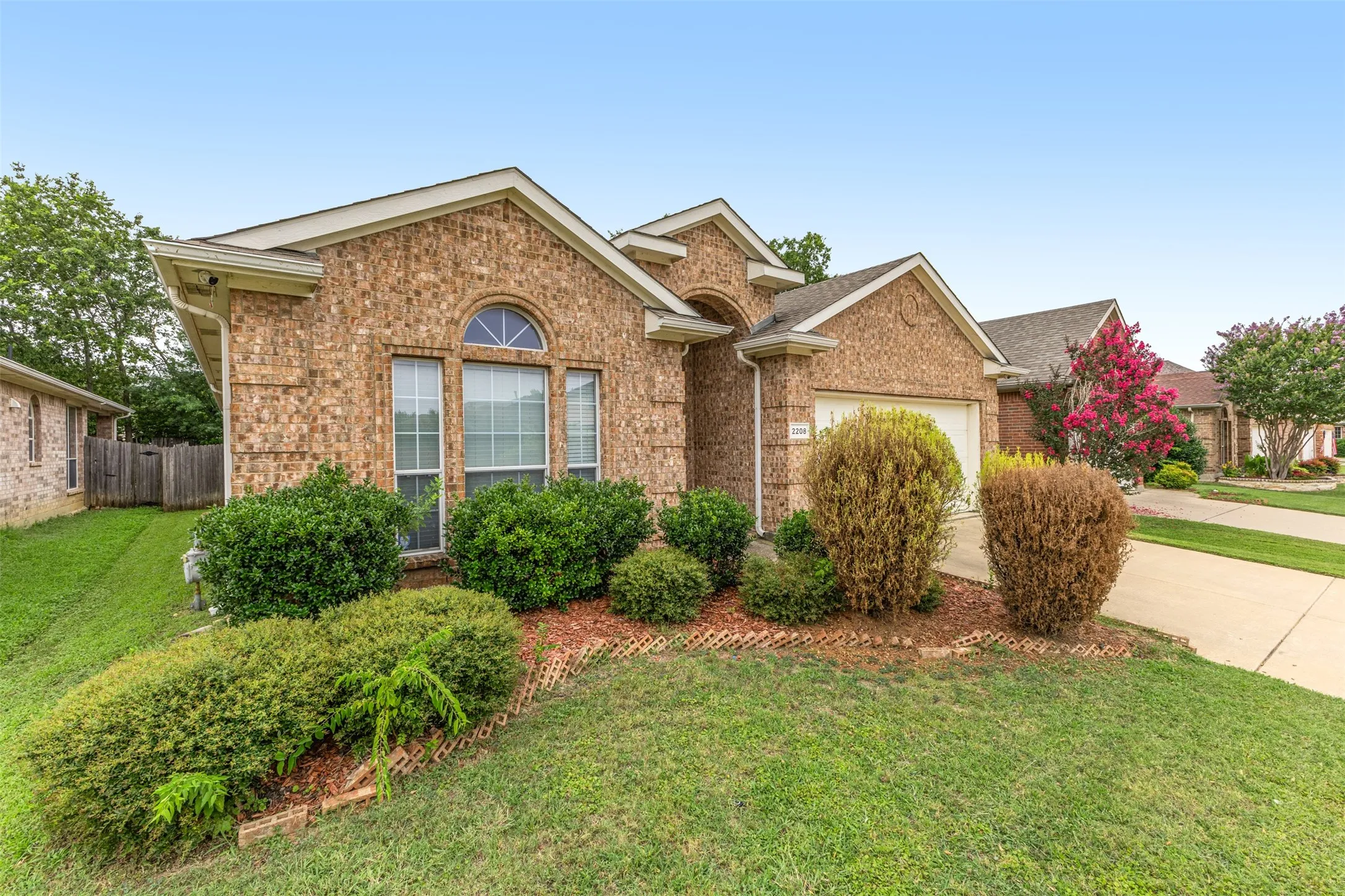 Brick exterior featuring an arched window, a two-car garage, and landscaped front planting beds