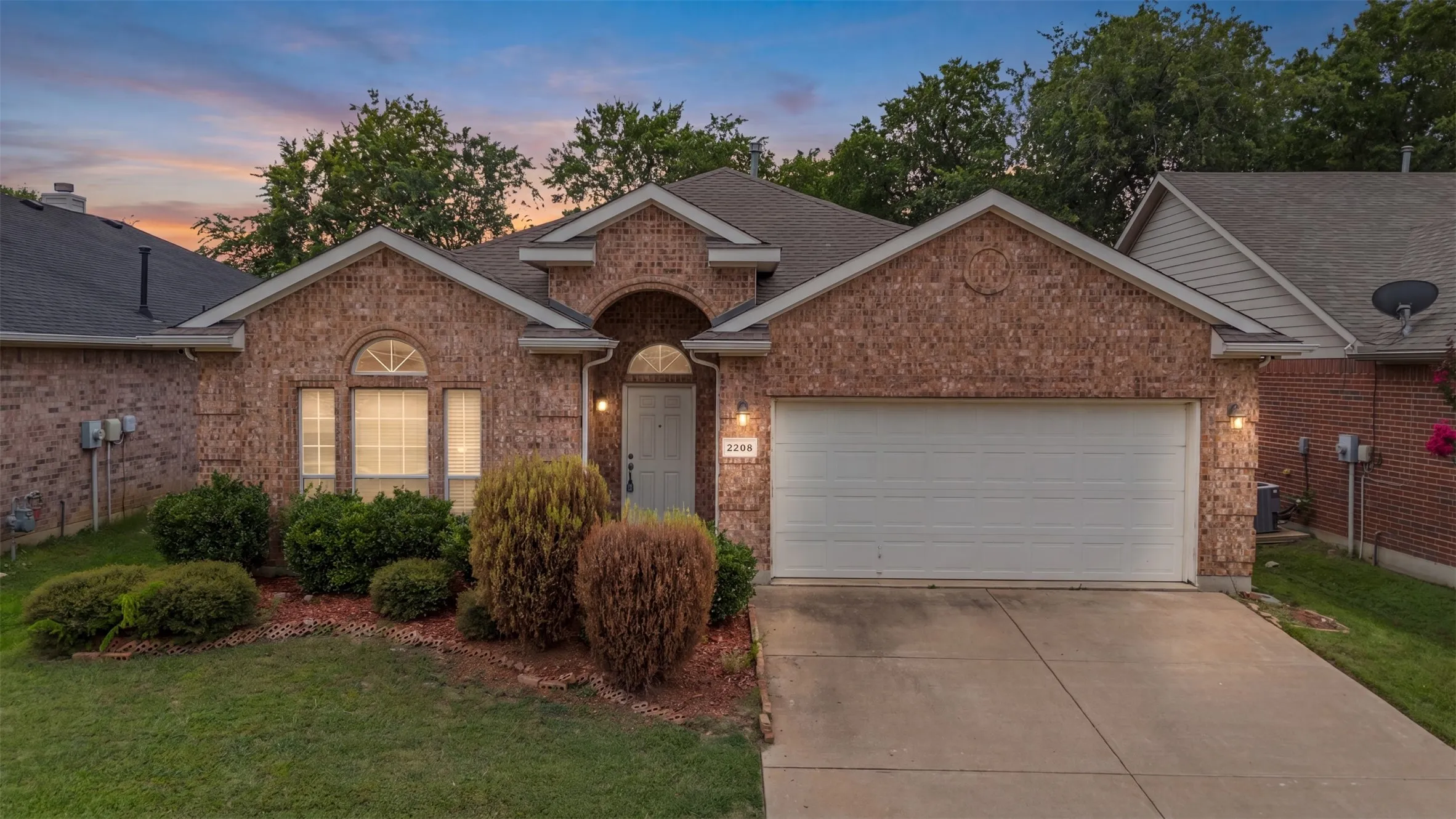 Brick-clad facade with an arched entry, a two-car garage, and established landscaping