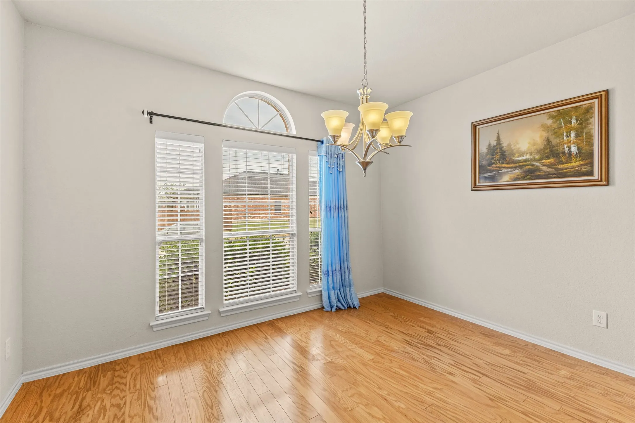 Room featuring wood-finish flooring, a multi-pane window with arched transom, and a chandelier with glass shades
