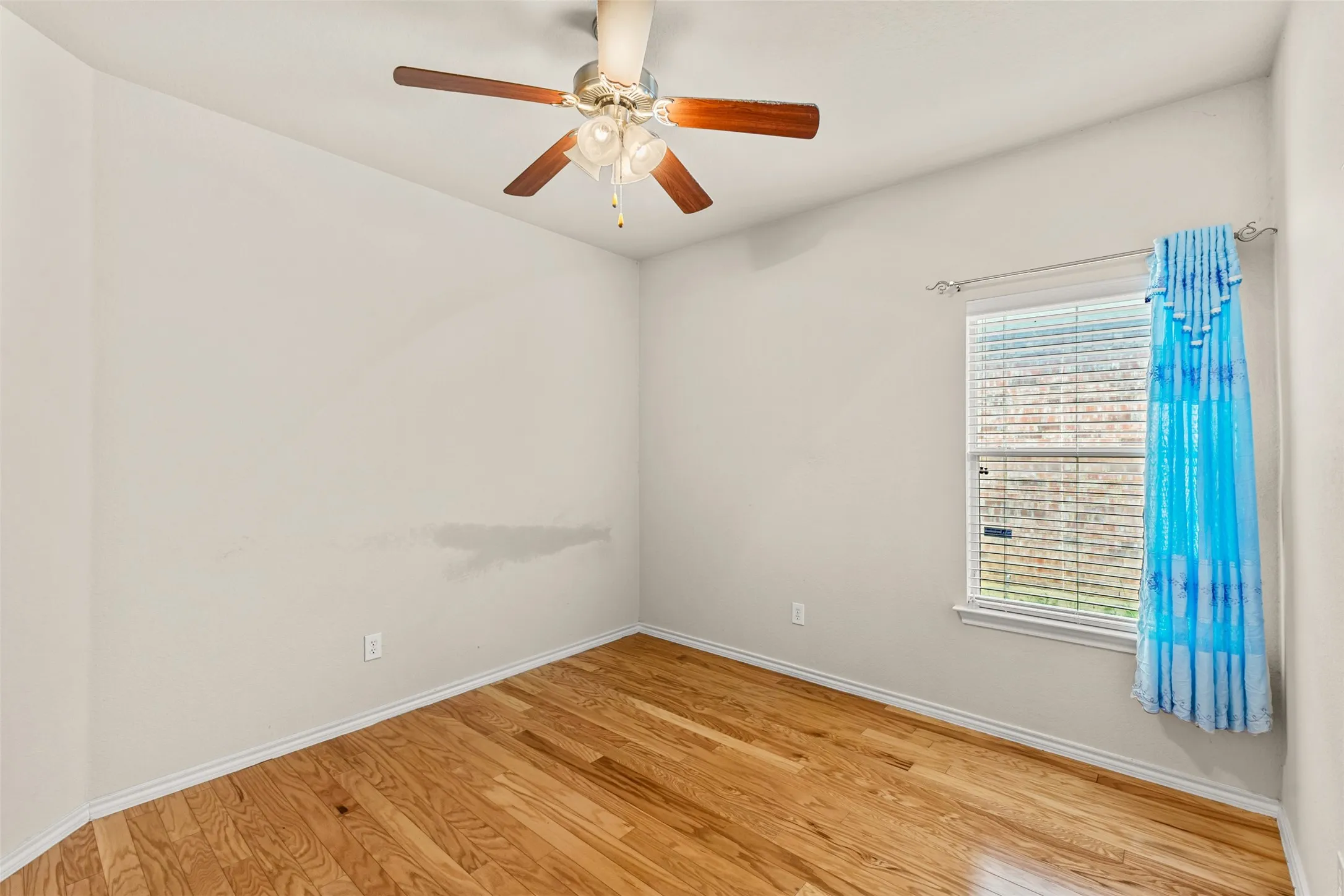 Wood-finish flooring with white baseboards, a window with blinds, and a ceiling fan with light fixture