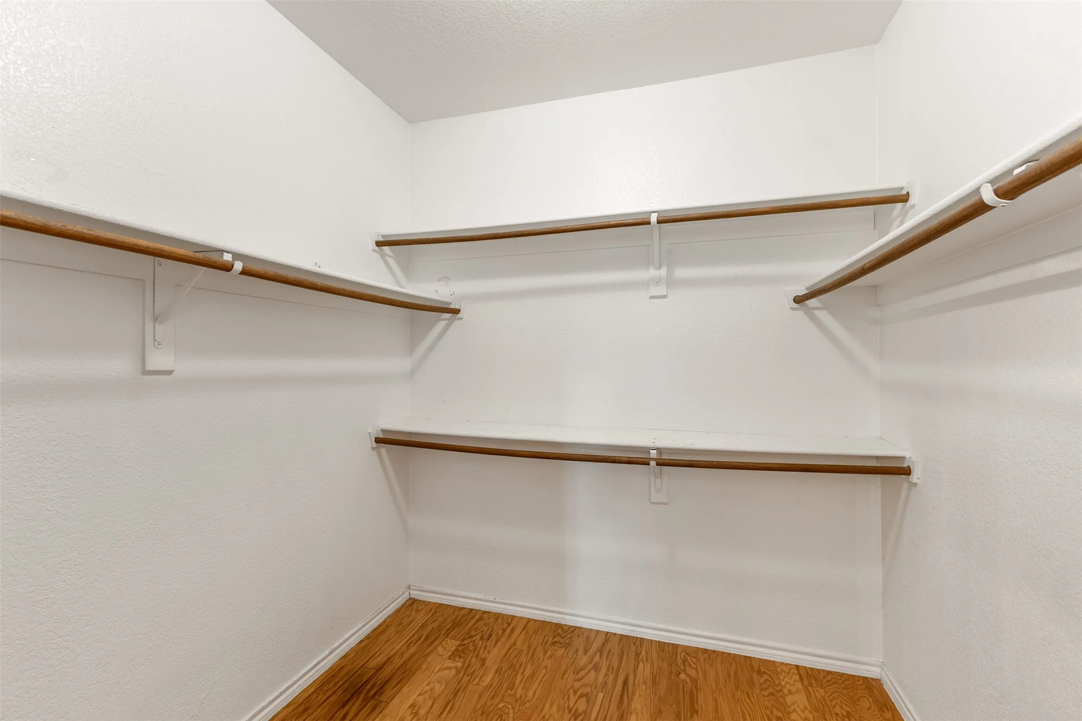 Walk-in closet featuring wood-finish flooring, white walls, and multiple built-in shelving units with hanging rods
