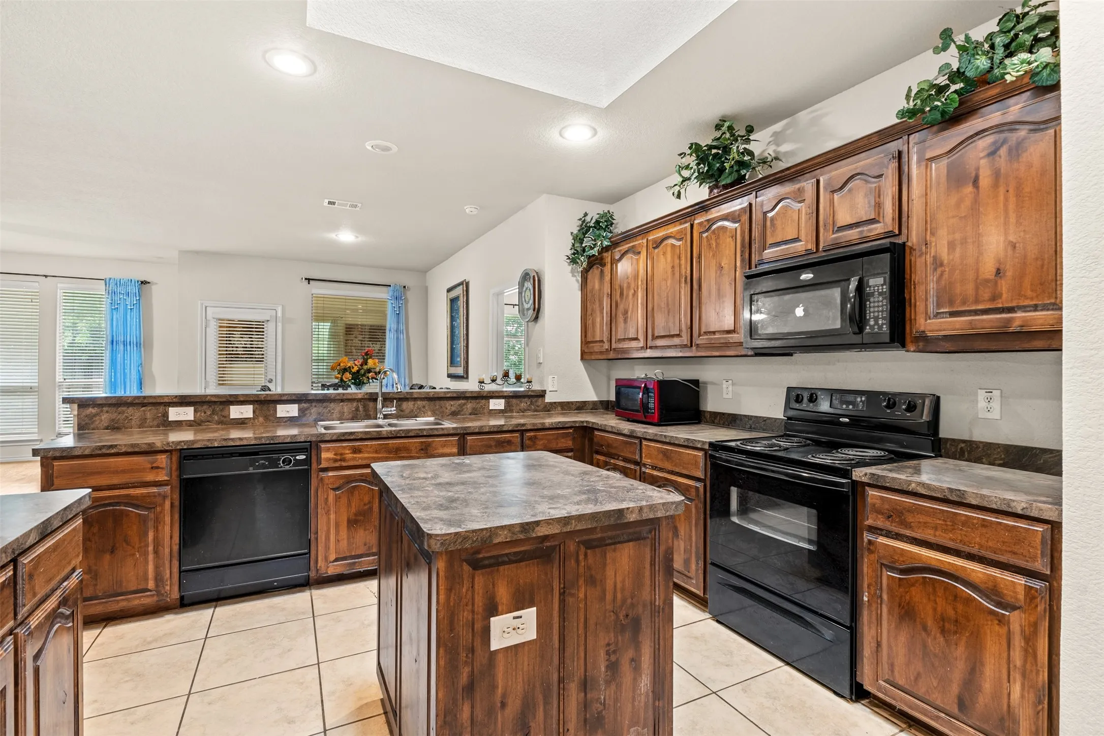 Kitchen featuring rich wood cabinetry, dark countertops, black appliances, a central island, and recessed lighting