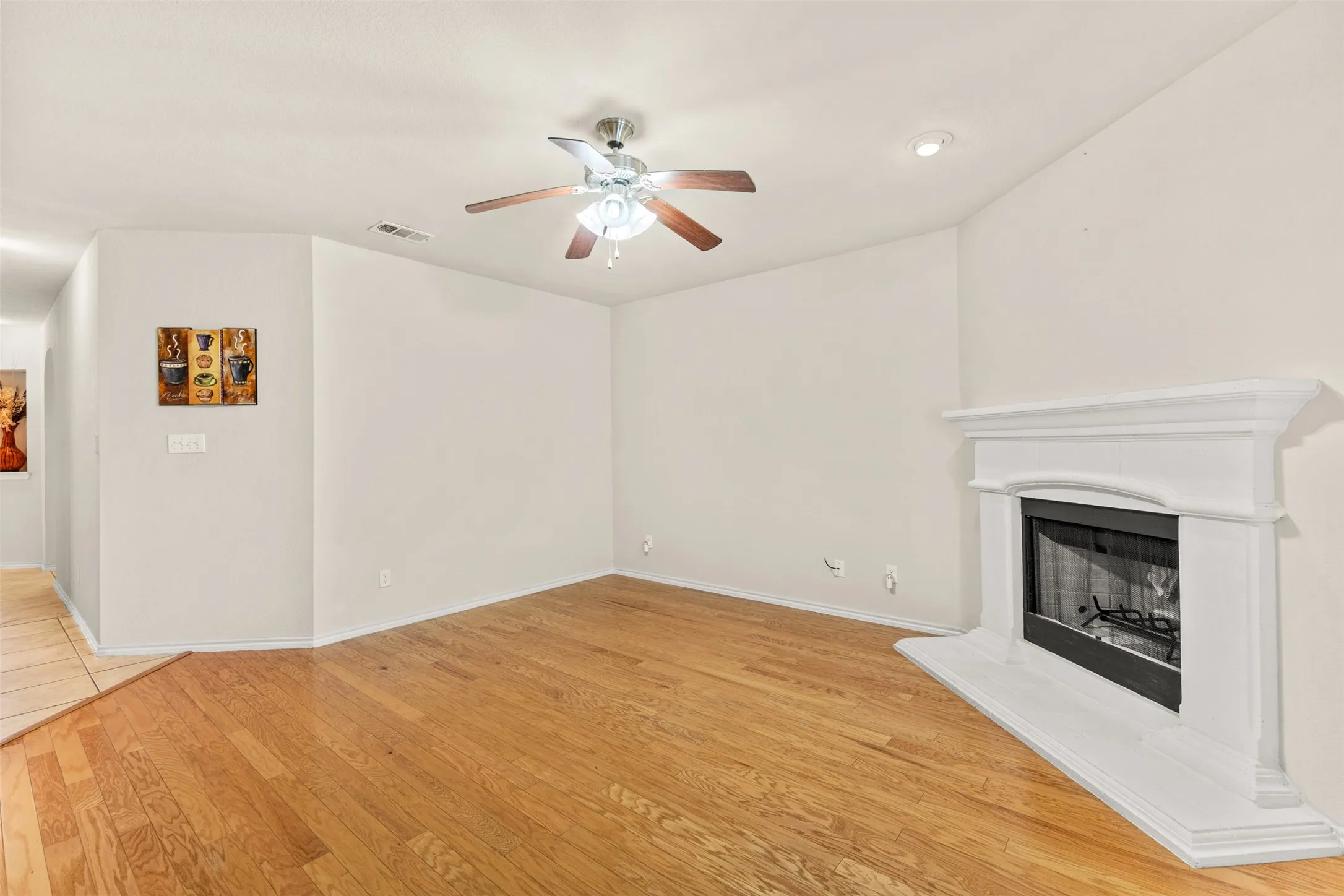 Spacious living area featuring wood-finish flooring, a white mantel fireplace, a ceiling fan with integrated lighting, and recessed lighting