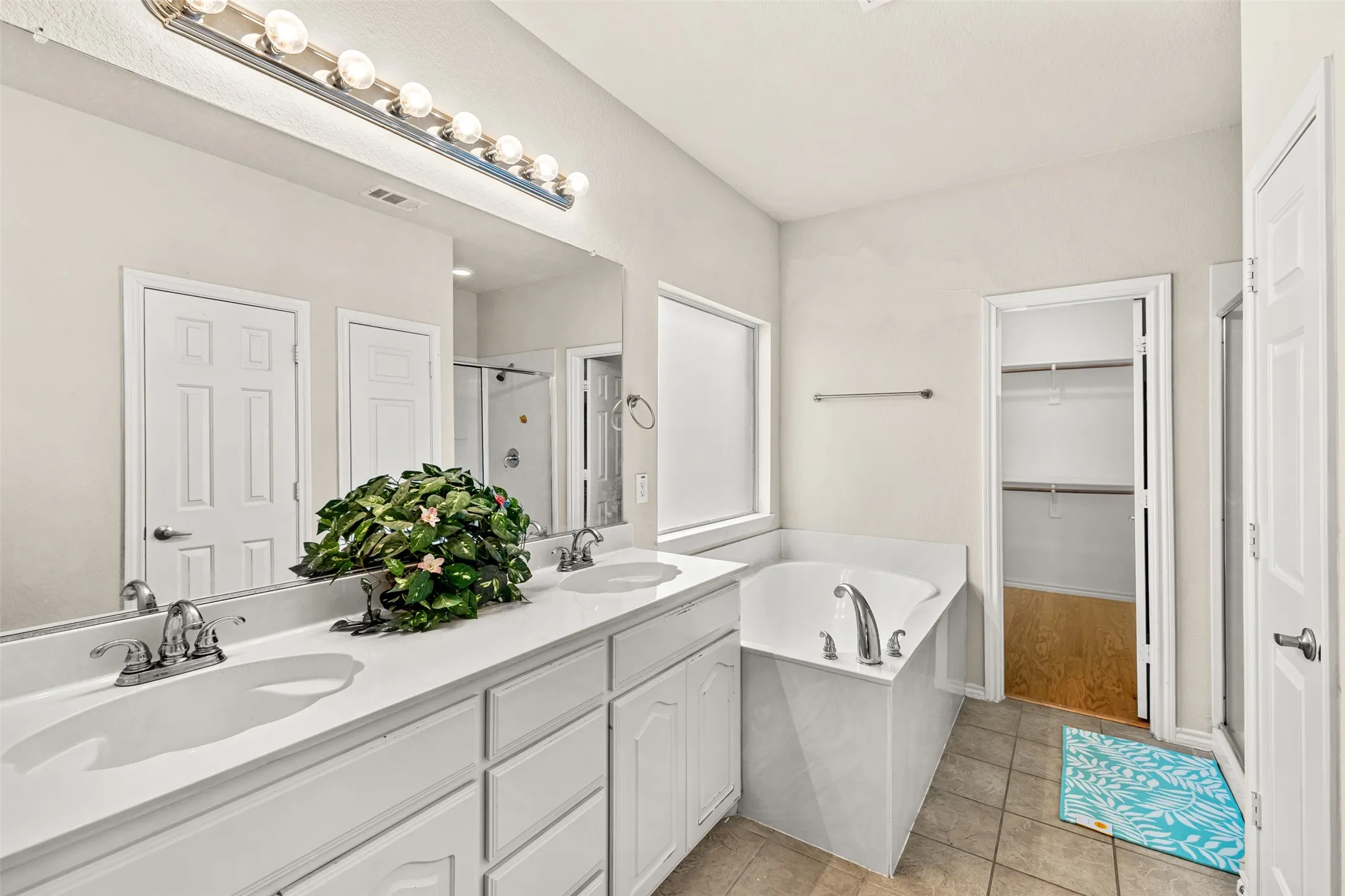 Bathroom featuring a double vanity with white cabinetry and integrated sinks, a built-in corner bathtub, a shower enclosure, and tile flooring