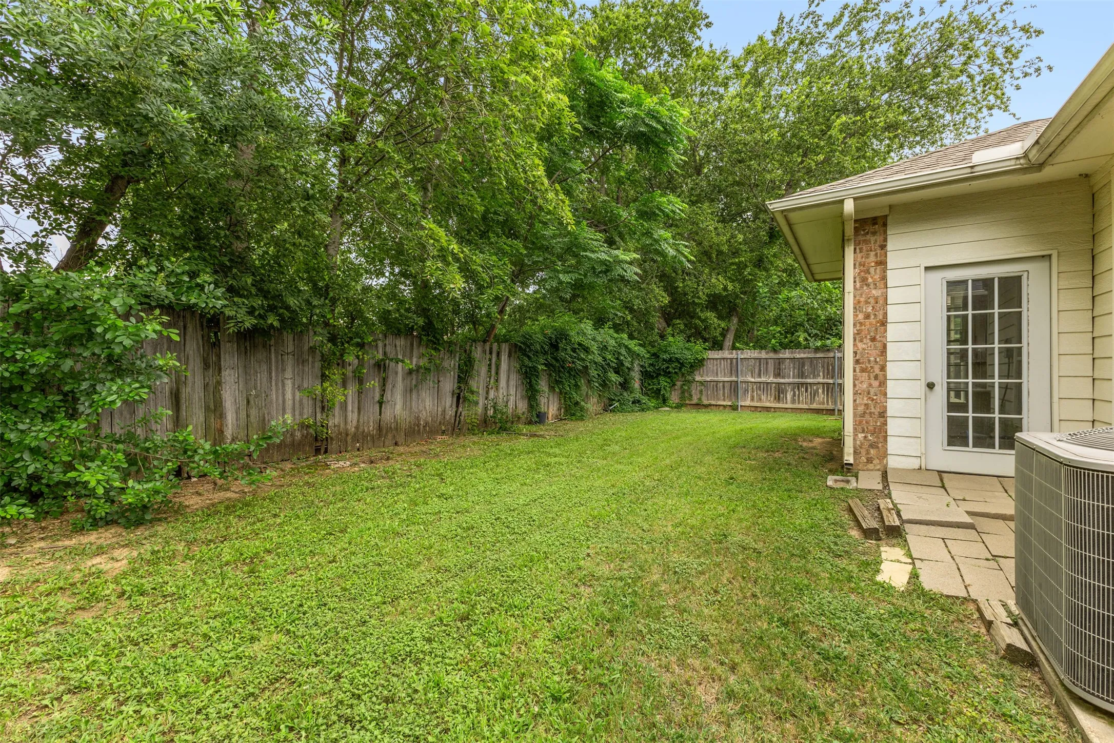 Spacious backyard featuring a grass lawn, privacy fencing, and mature trees