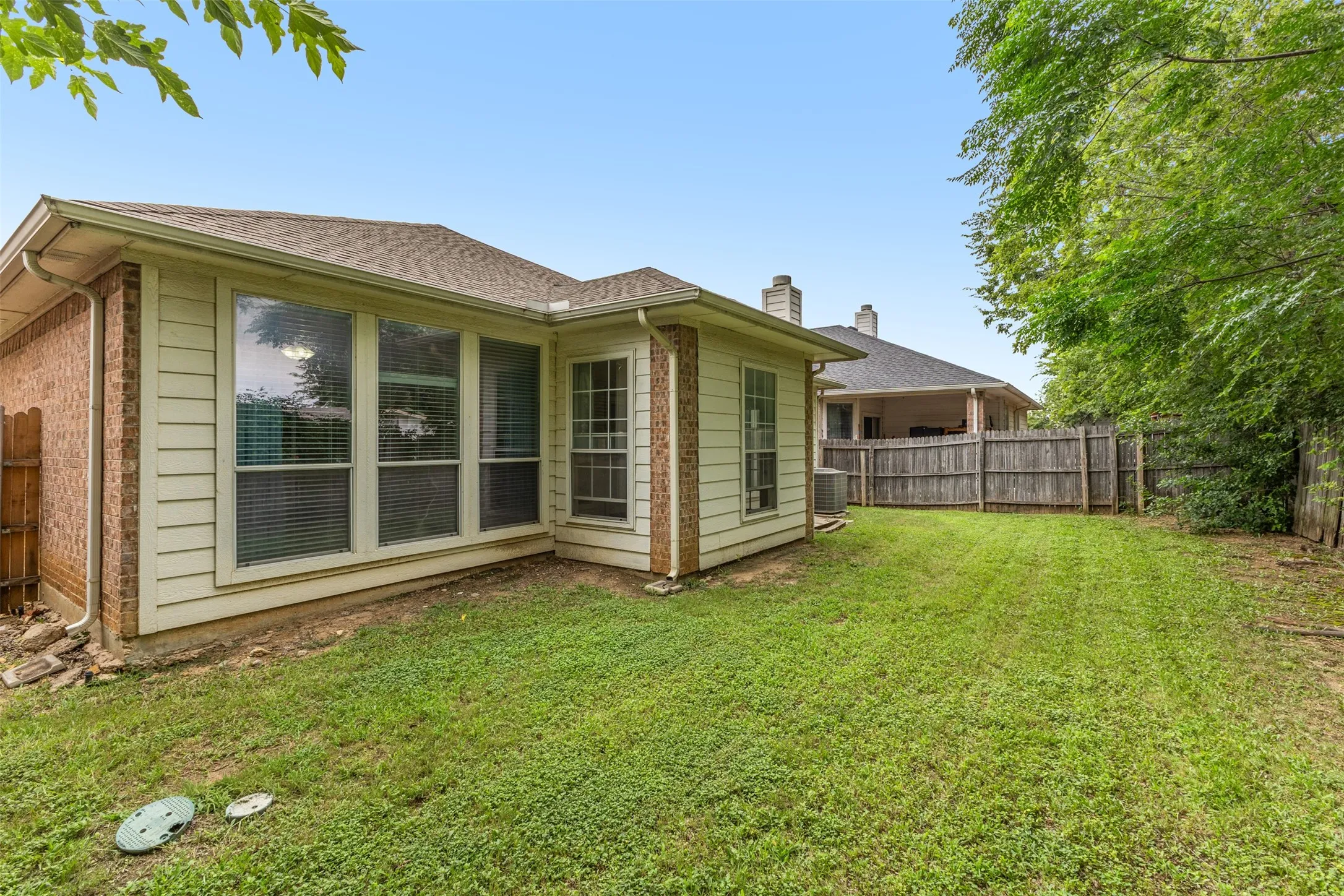 Expansive backyard featuring a manicured lawn, wood fencing, and mature trees