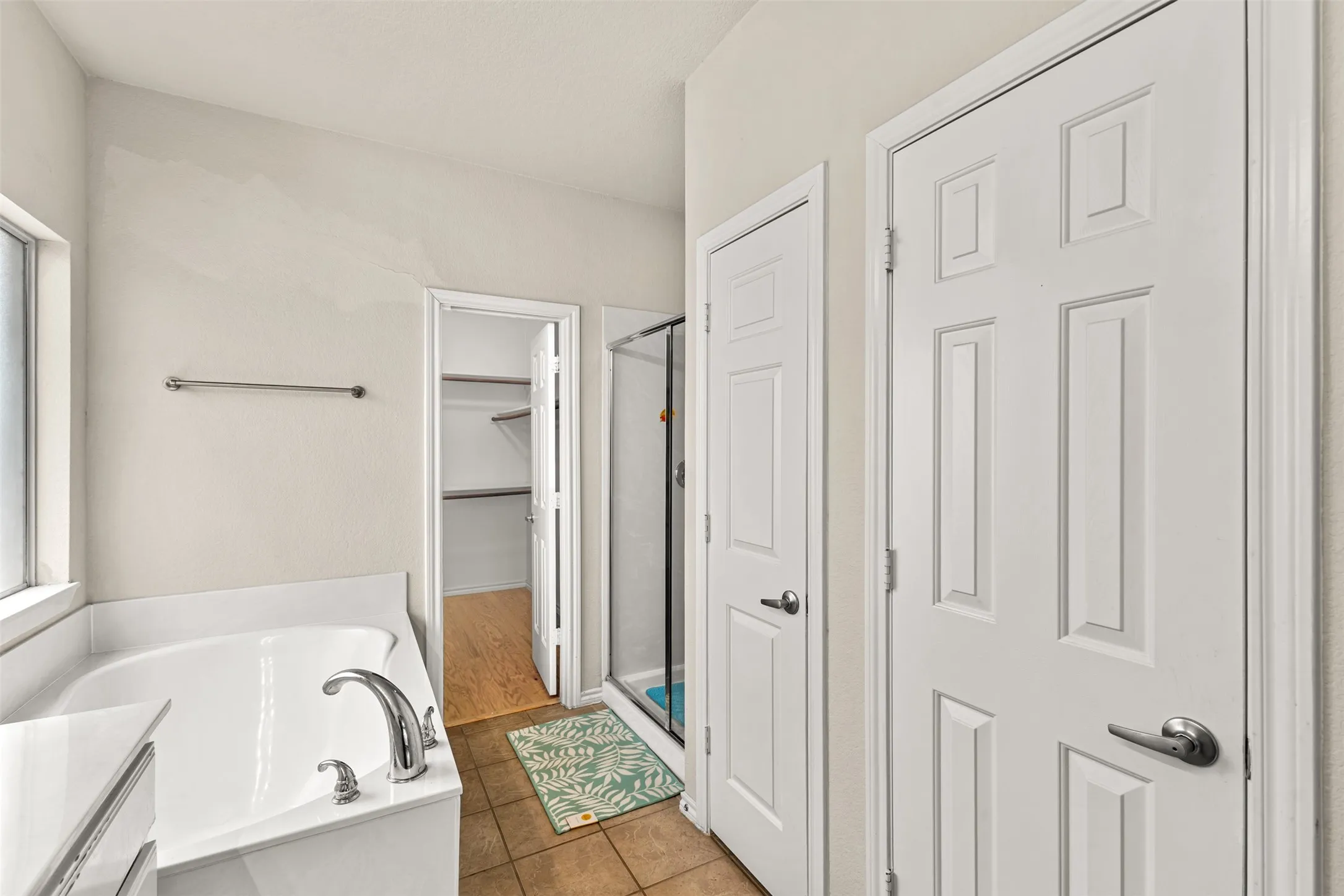 Bathroom featuring a built-in soaking tub with chrome fixtures, a separate glass-enclosed shower, and neutral-toned tile flooring