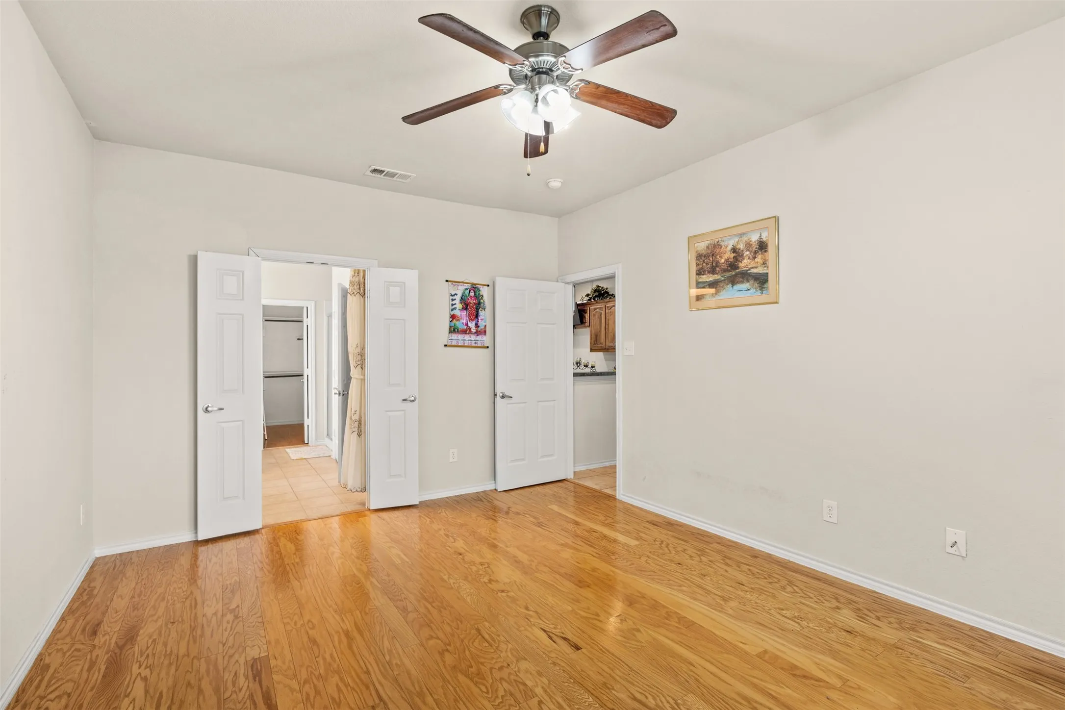 Spacious room featuring wood-finish flooring, light-toned walls, and a ceiling fan with integrated lighting