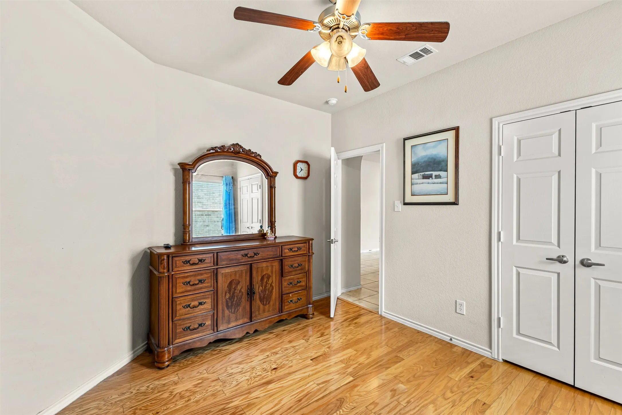 Wood-finish flooring throughout, featuring a ceiling fan with light fixture, light-toned walls, and a pair of white paneled doors