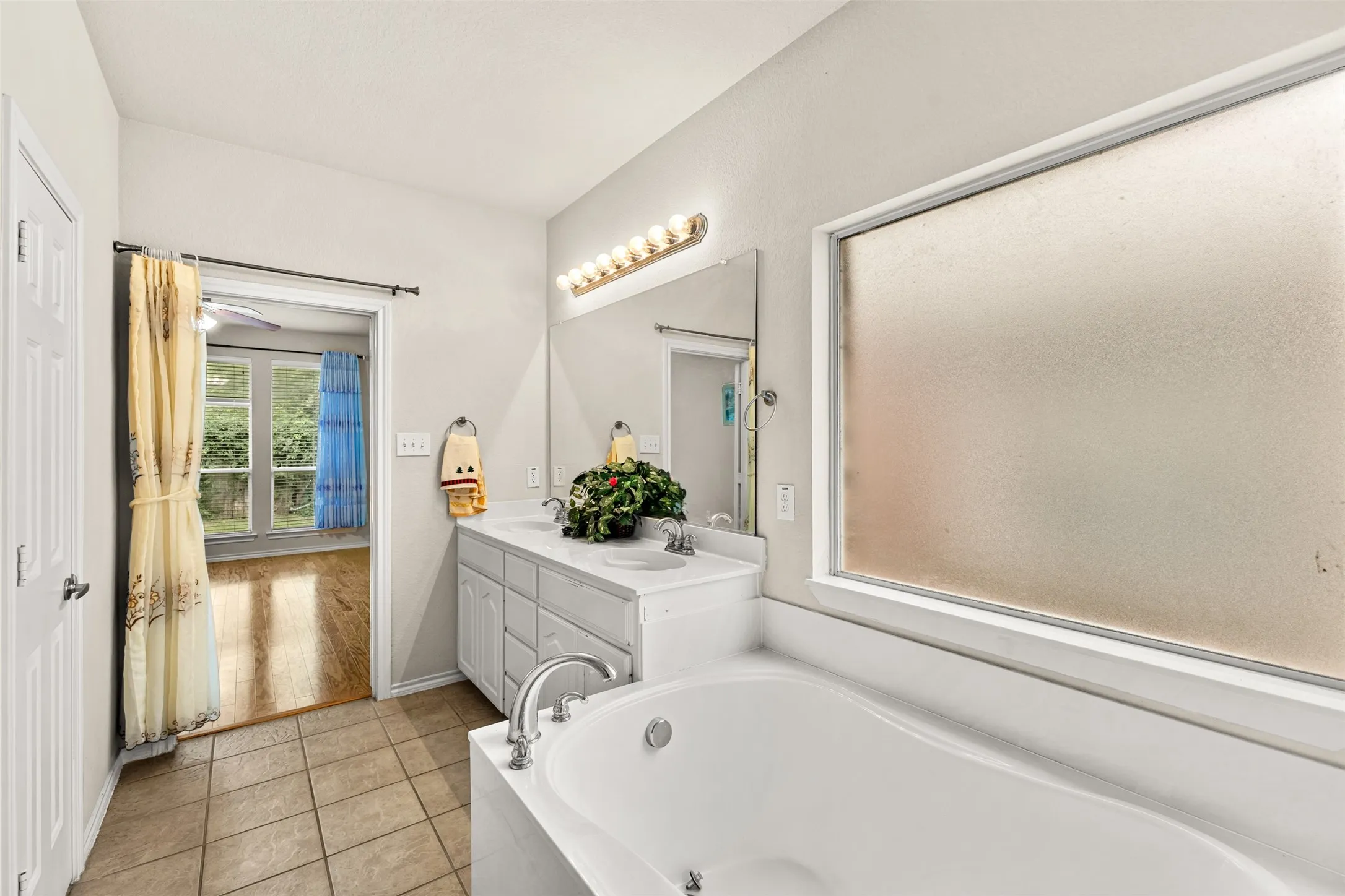 Bathroom featuring a built-in tub, dual sink vanity with mirrors and vanity lighting, and tiled flooring