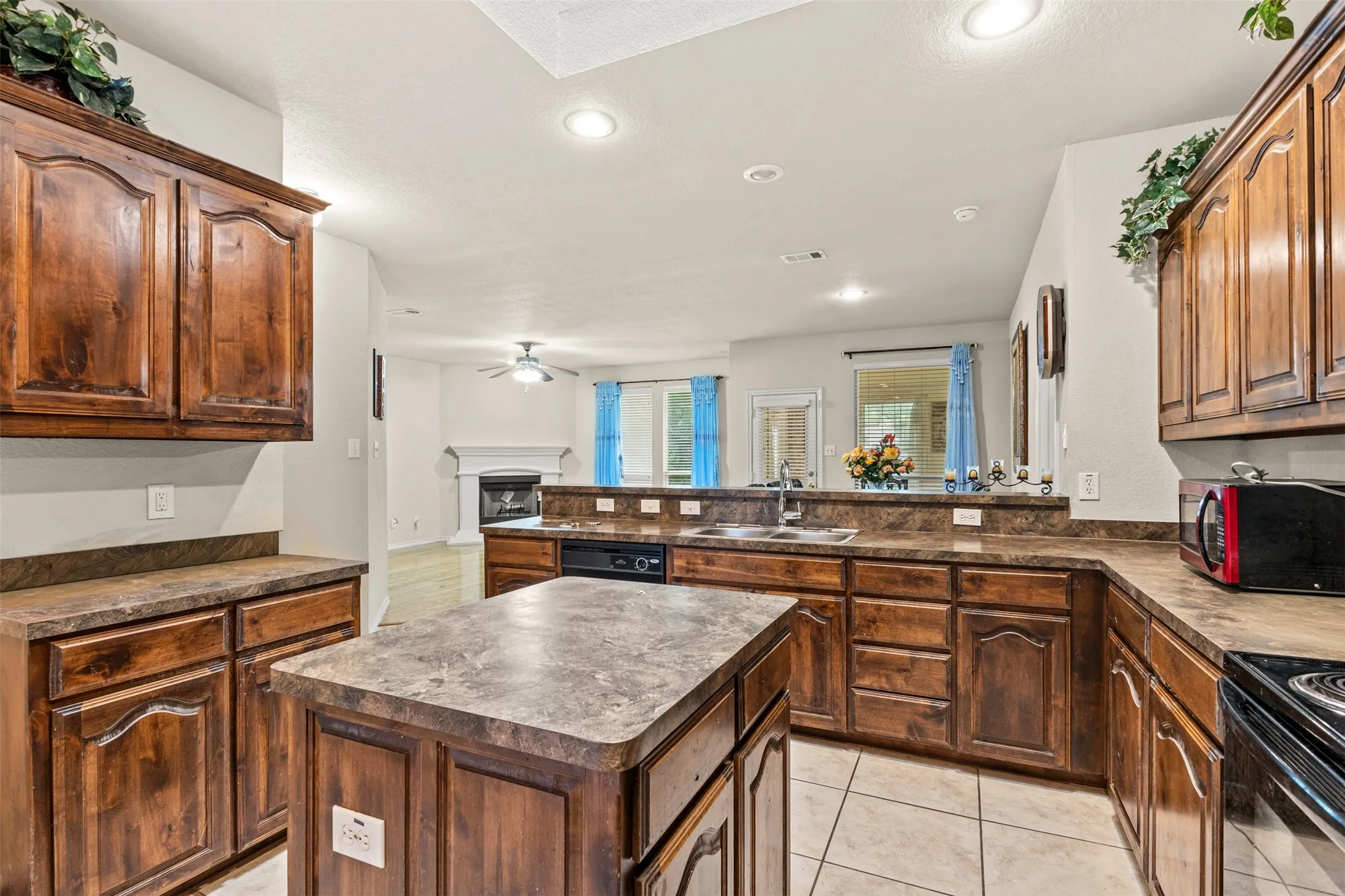 Kitchen featuring a central island, wood cabinetry, stone-finish countertops, stainless steel sink, and tile flooring