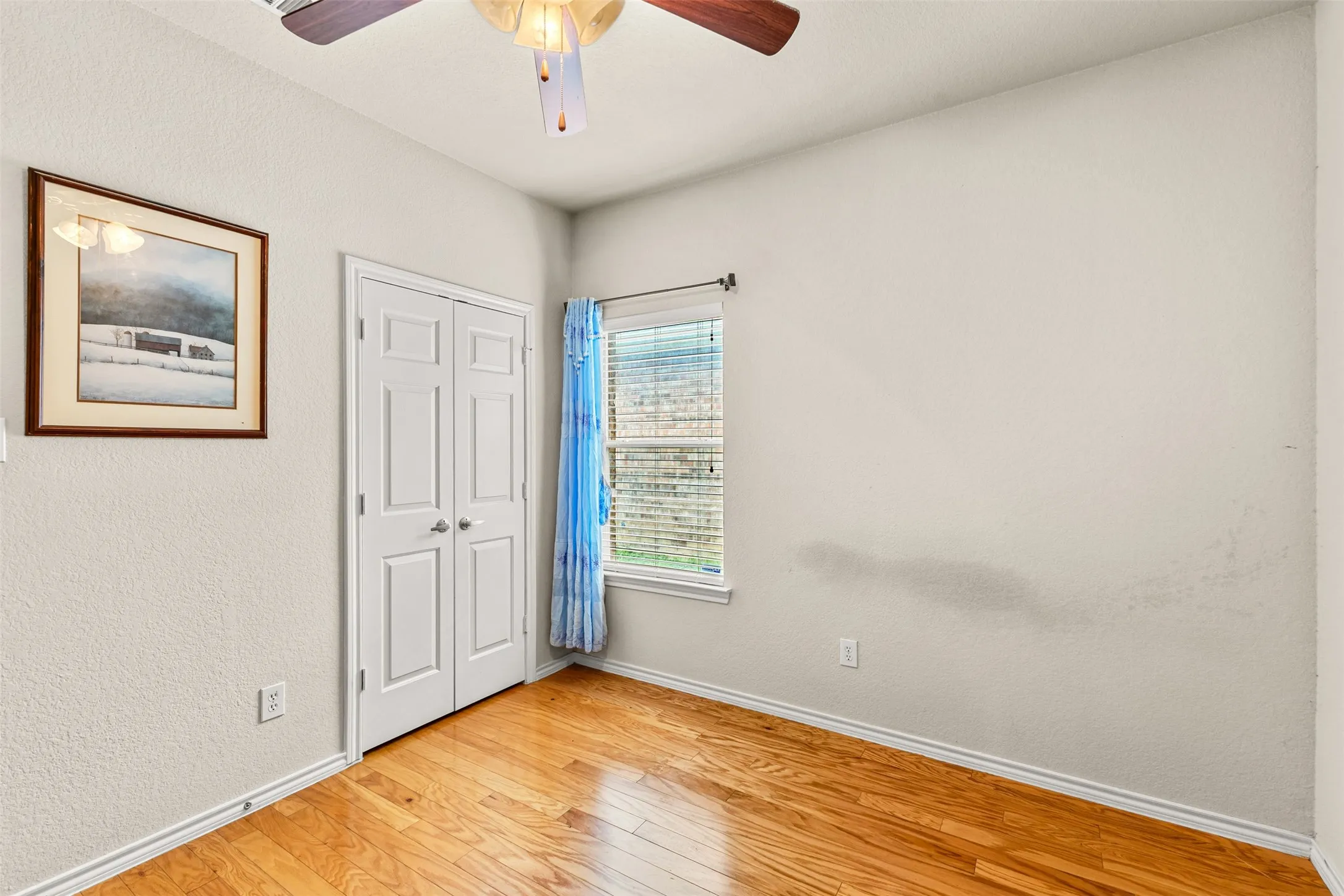 Interior room featuring wood-finish flooring, a double-door closet, and a ceiling fan with integrated lighting