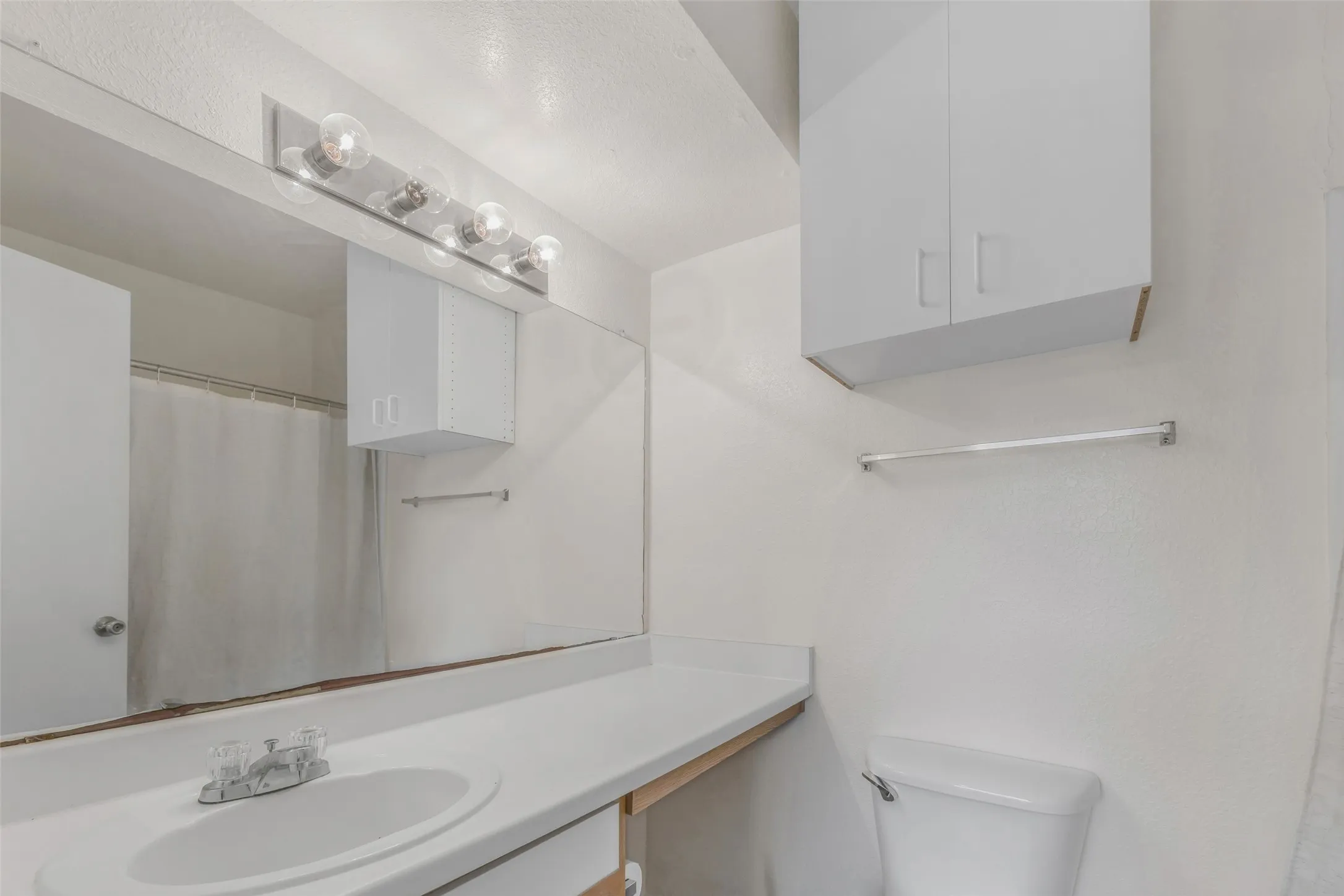 Bathroom featuring an elongated vanity with an integrated sink, a large mirror, and overhead vanity lighting