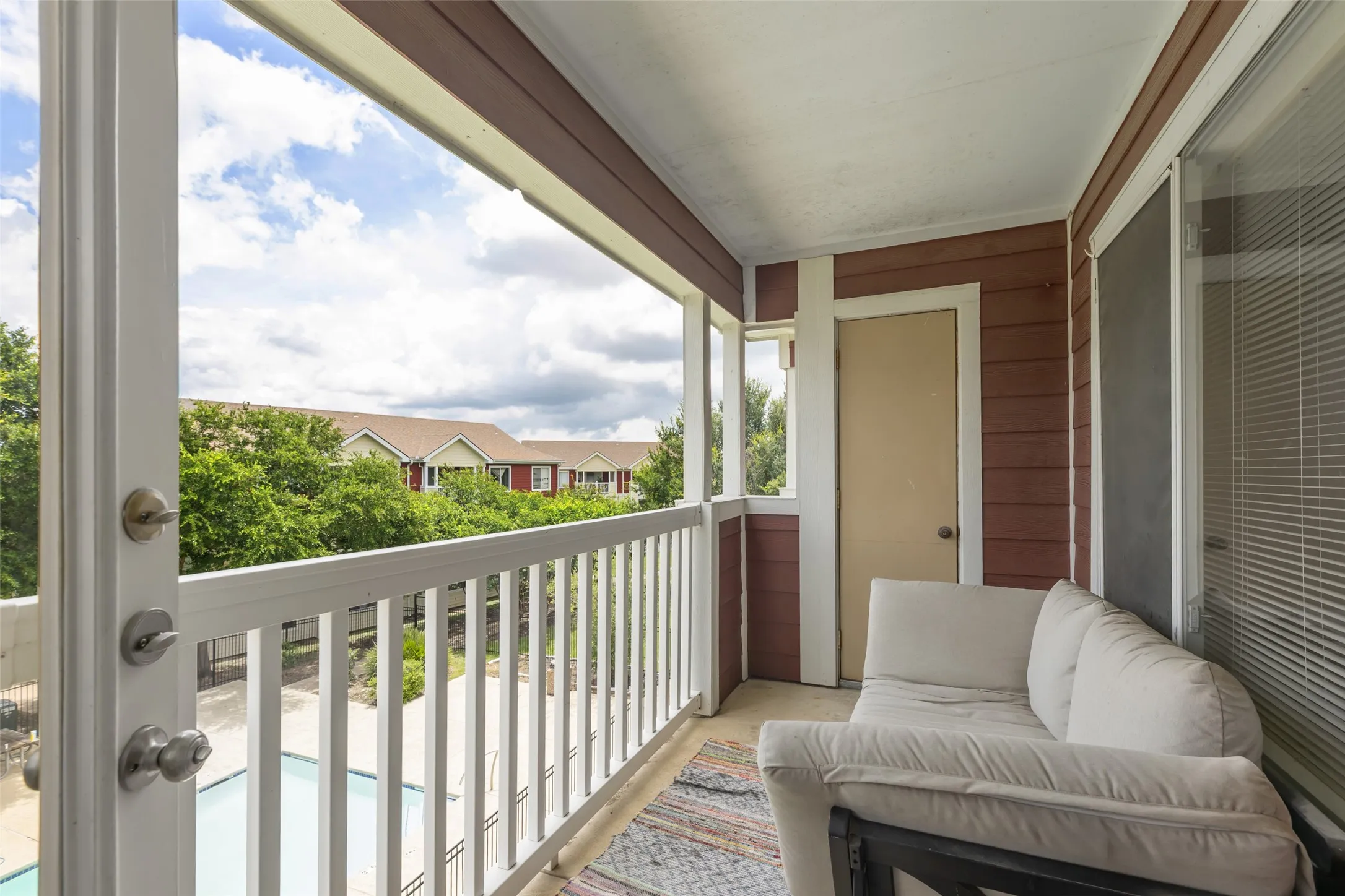 Covered balcony featuring wood-finish siding, white railing, and concrete flooring. Balcony overlooks the pool.