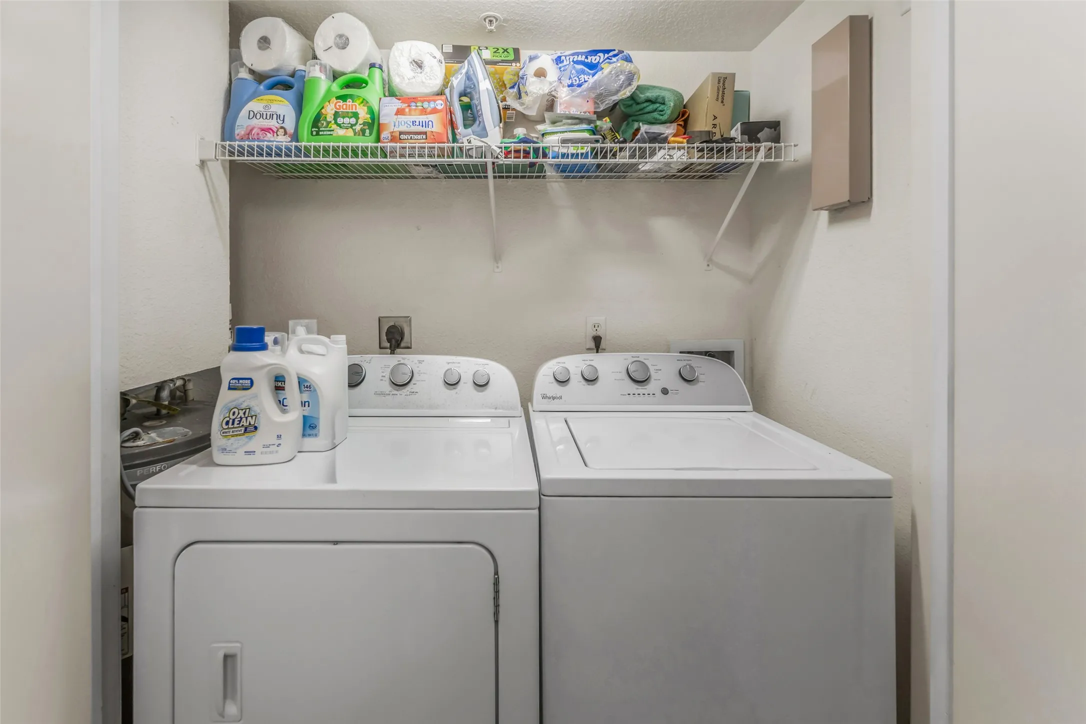 Dedicated laundry area featuring a white washer and dryer pair, an overhead wire shelving unit, and wall-mounted utility hookups