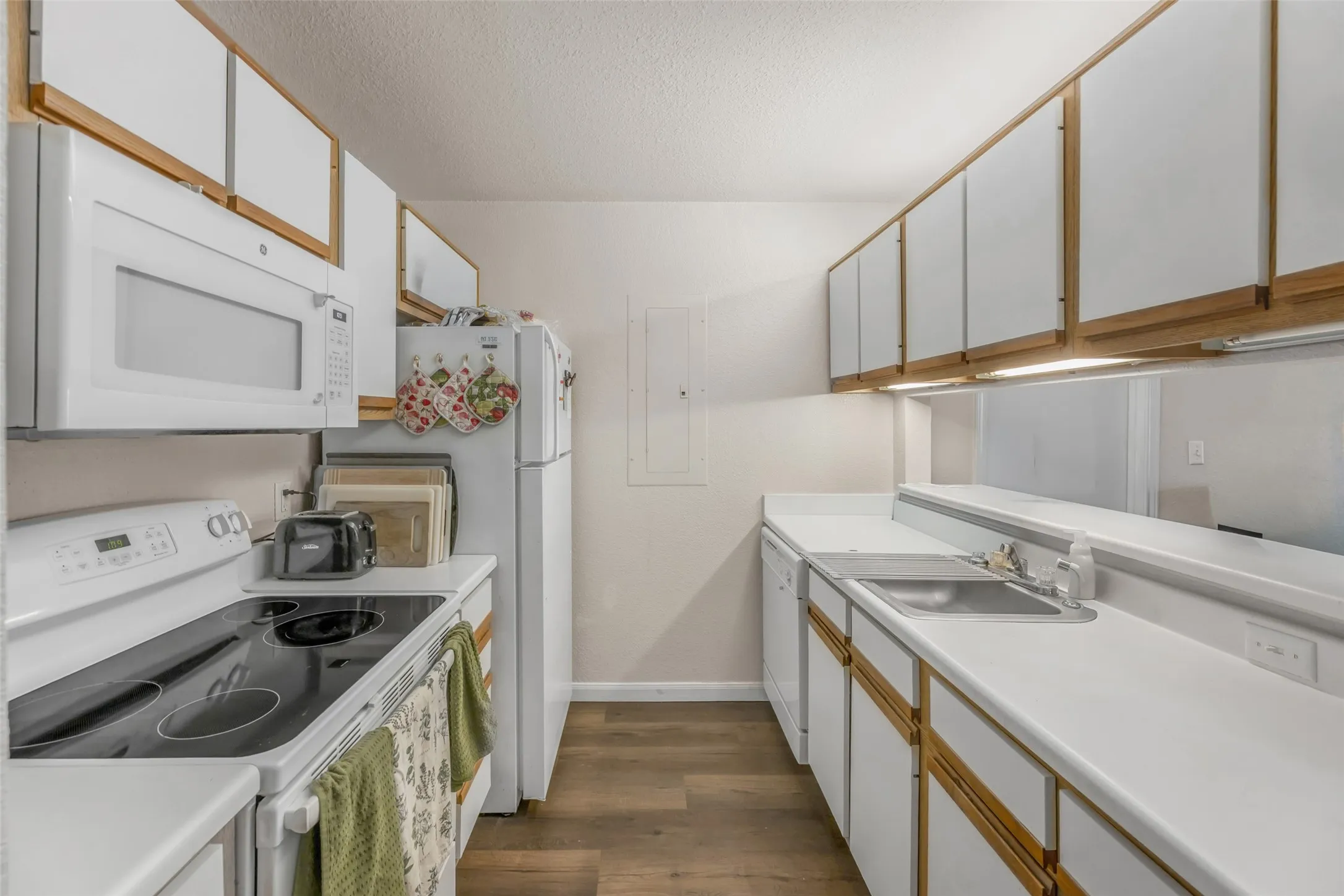 Galley kitchen featuring white cabinetry with wood-finish trim, white appliances including an oven range and microwave, light-toned countertops.