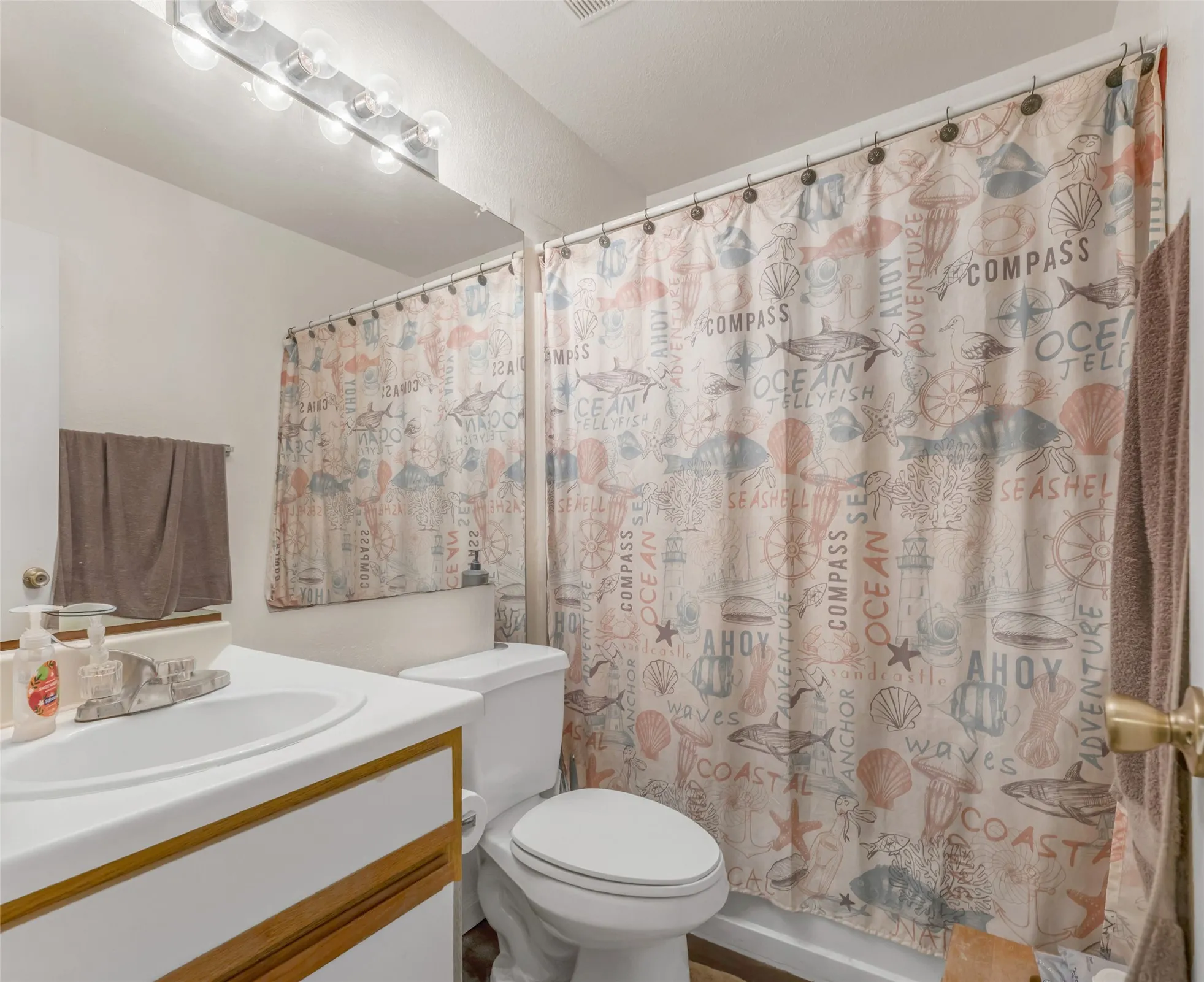 Bathroom features a single vanity with a white countertop and integrated sink, a commode, and a shower/tub combination