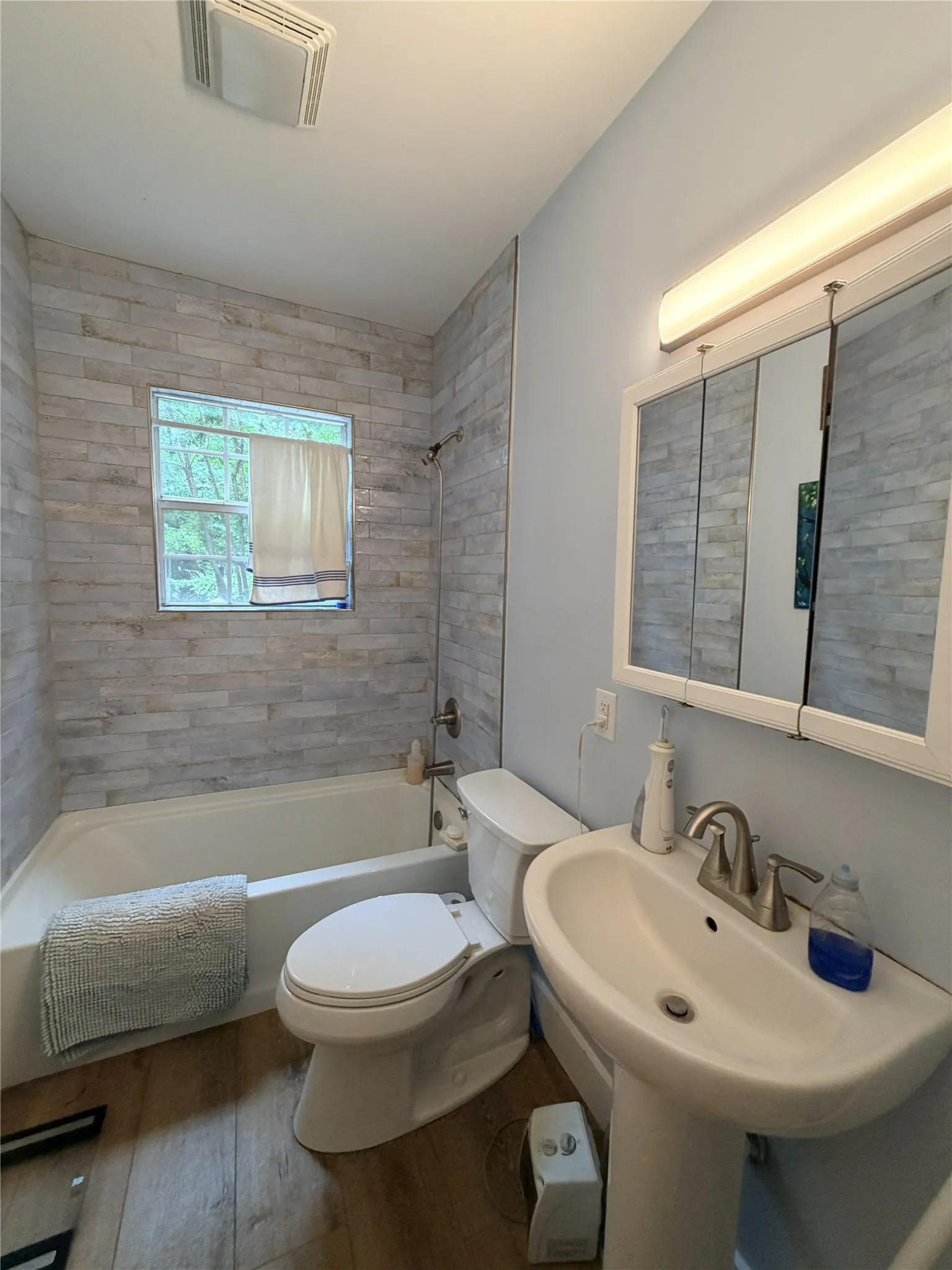 Bathroom featuring a white pedestal sink, brushed nickel faucet, and a wall-mounted medicine cabinet with integrated lighting