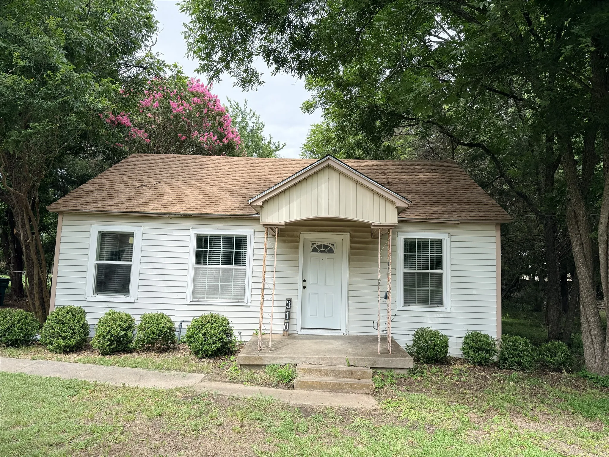 White siding exterior with a pitched shingle roof, covered entry, and decorative front door