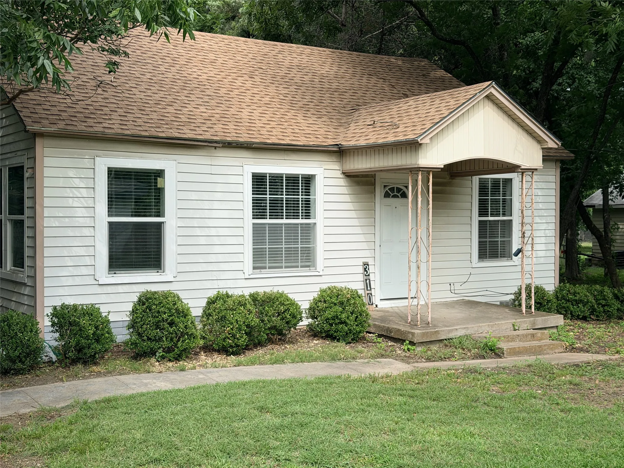Light-colored siding exterior with a pitched roof, front porch with decorative columns, white-framed windows, and established shrubbery