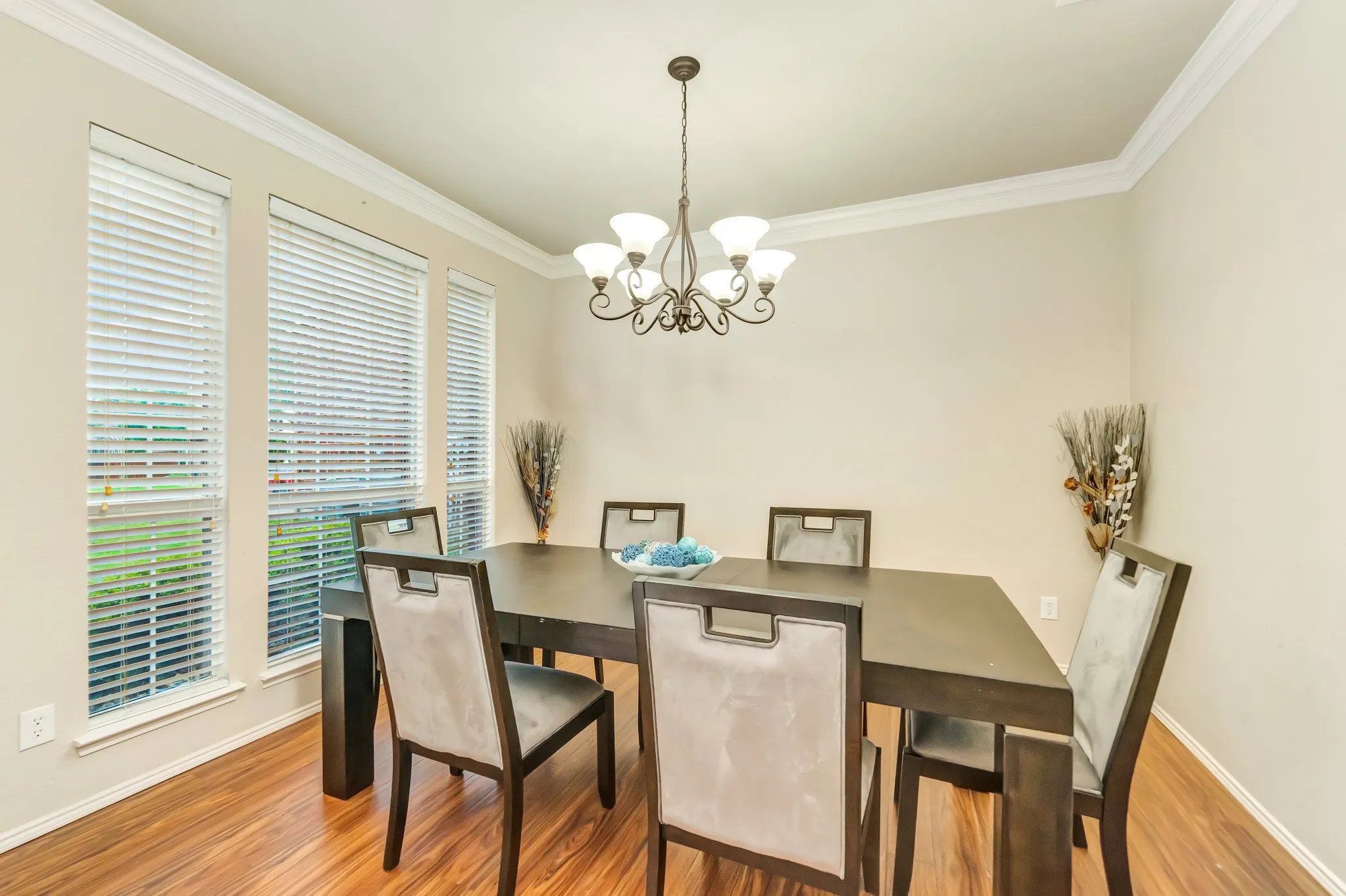 Formal dining area featuring rich wood-finish flooring, multiple windows with blinds, and a decorative chandelier