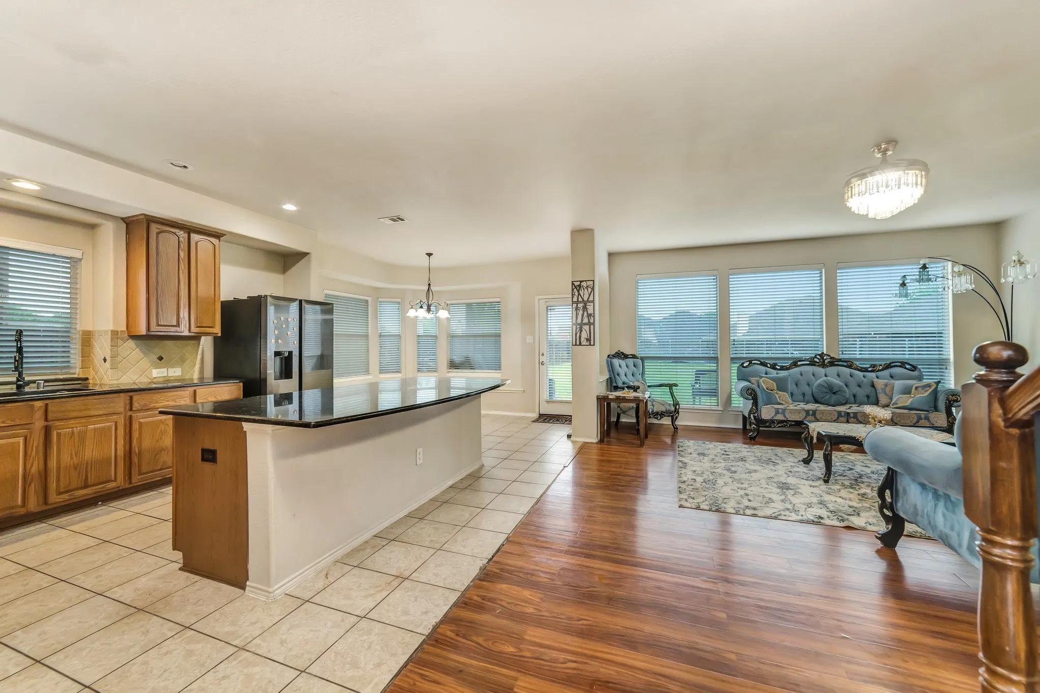 Open-concept living space featuring wood-finish flooring, a kitchen island with a dark countertop, wood cabinetry, a tile backsplash, and a stainless steel refrigerator
