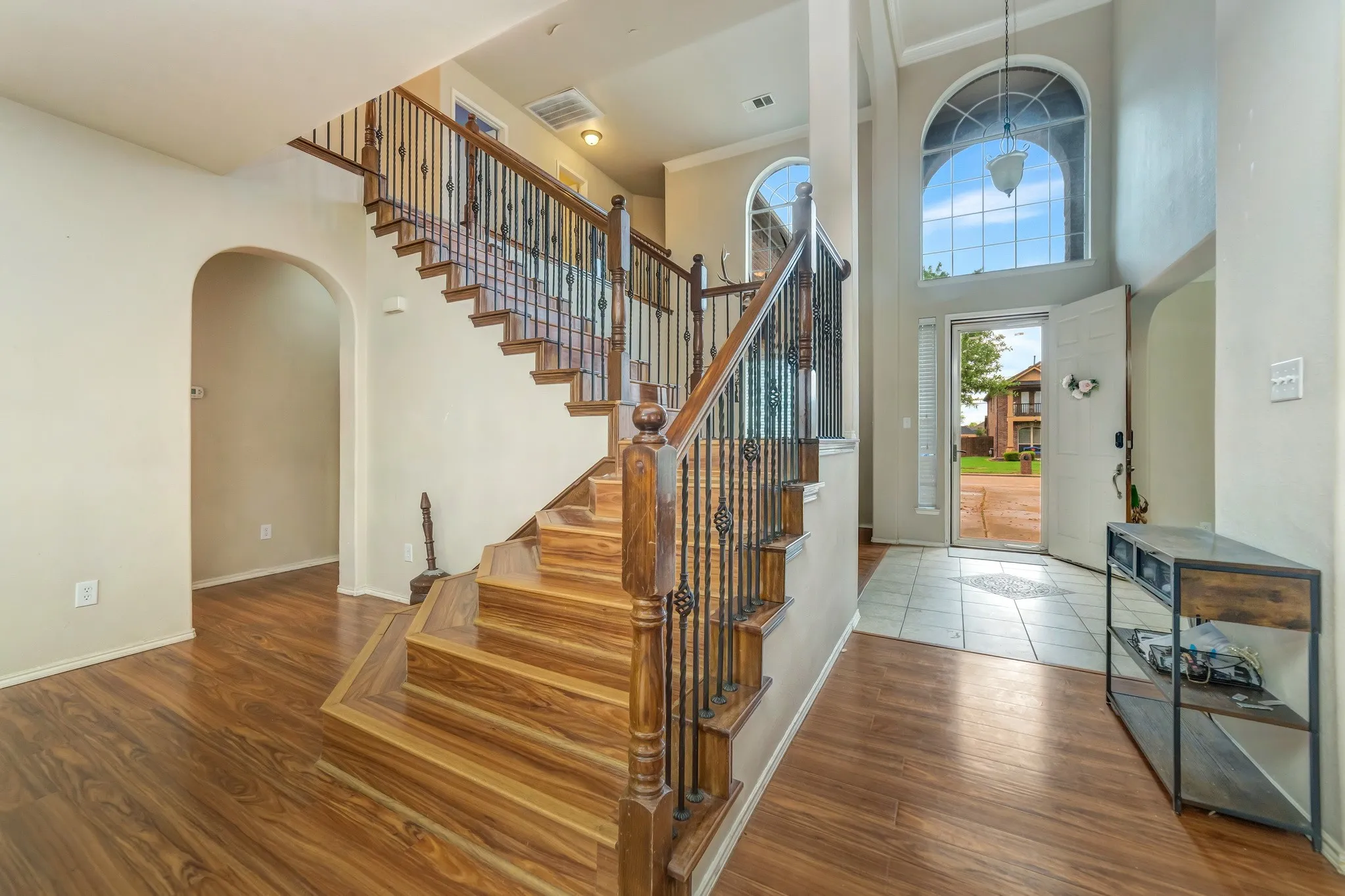 Double-height foyer featuring a large arched window with transom, wood-finish flooring, and a staircase with wrought iron balusters