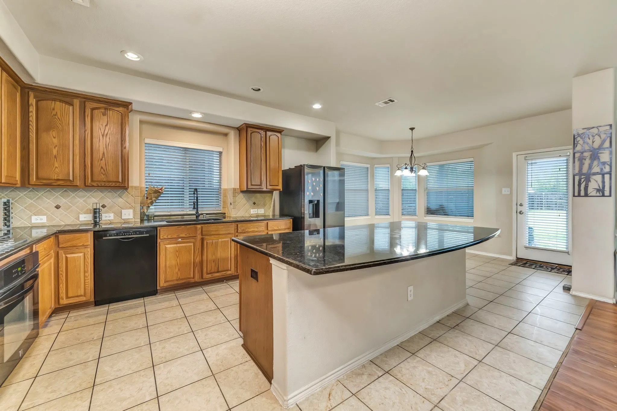 Expansive kitchen featuring a large central island with a dark countertop, light wood cabinetry, a built-in refrigerator, and a bay window