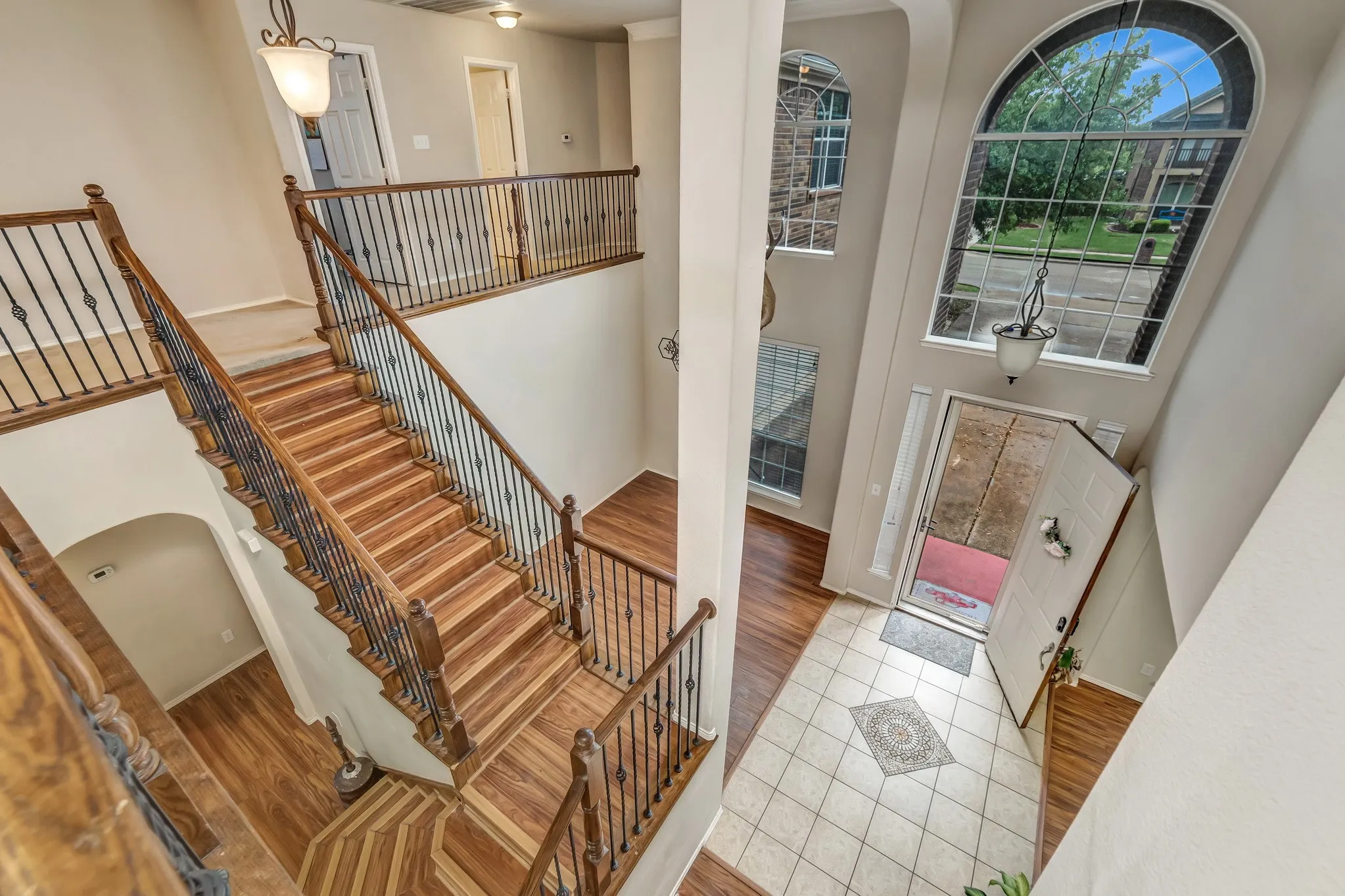 Grand entry featuring a two-story foyer with an arched window, a prominent wood-finish staircase with wrought iron balusters, and a tiled entryway with an inlaid accent