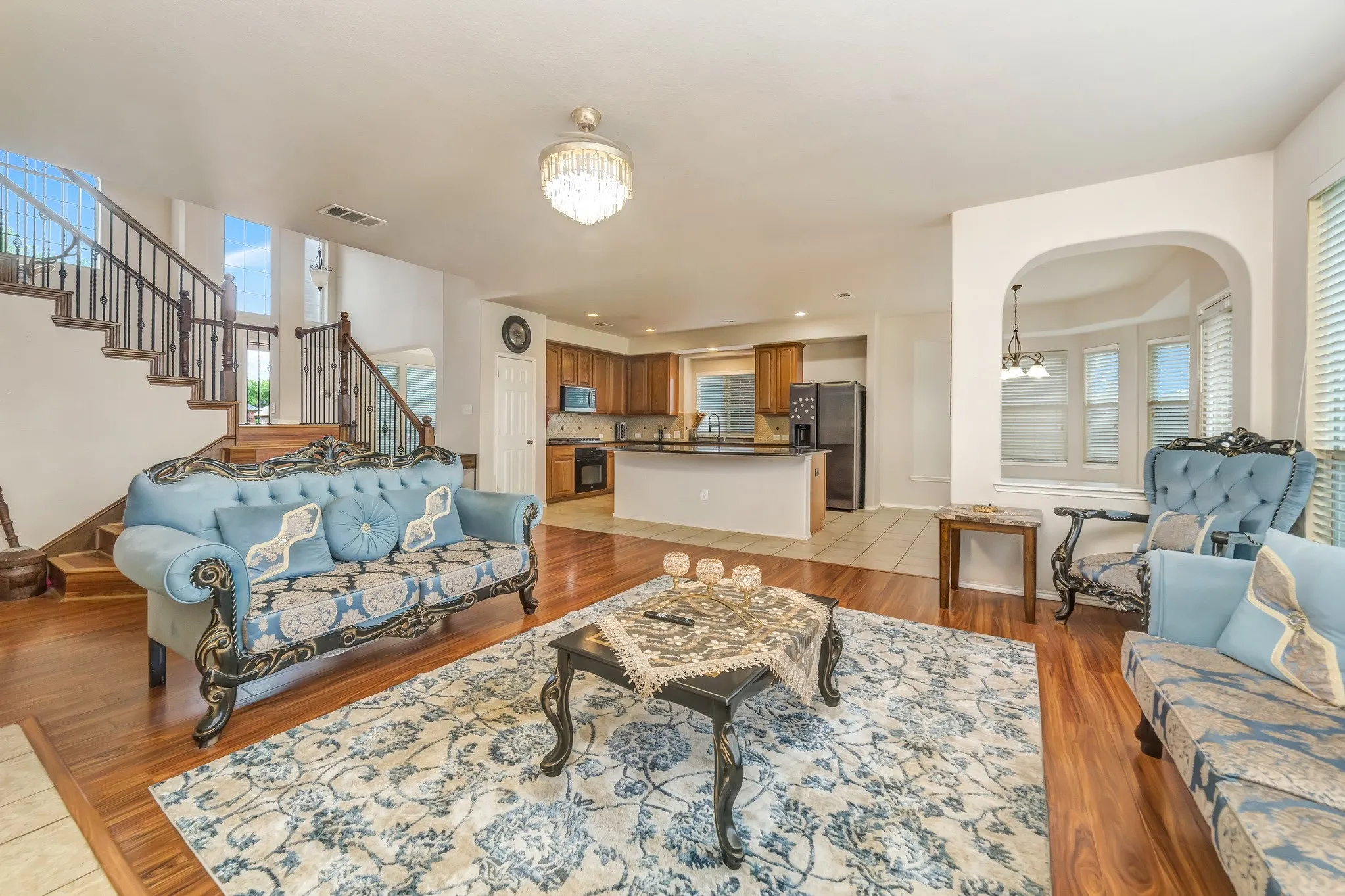 Spacious living area featuring wood-finish flooring, a two-story ceiling, and an open layout to the kitchen