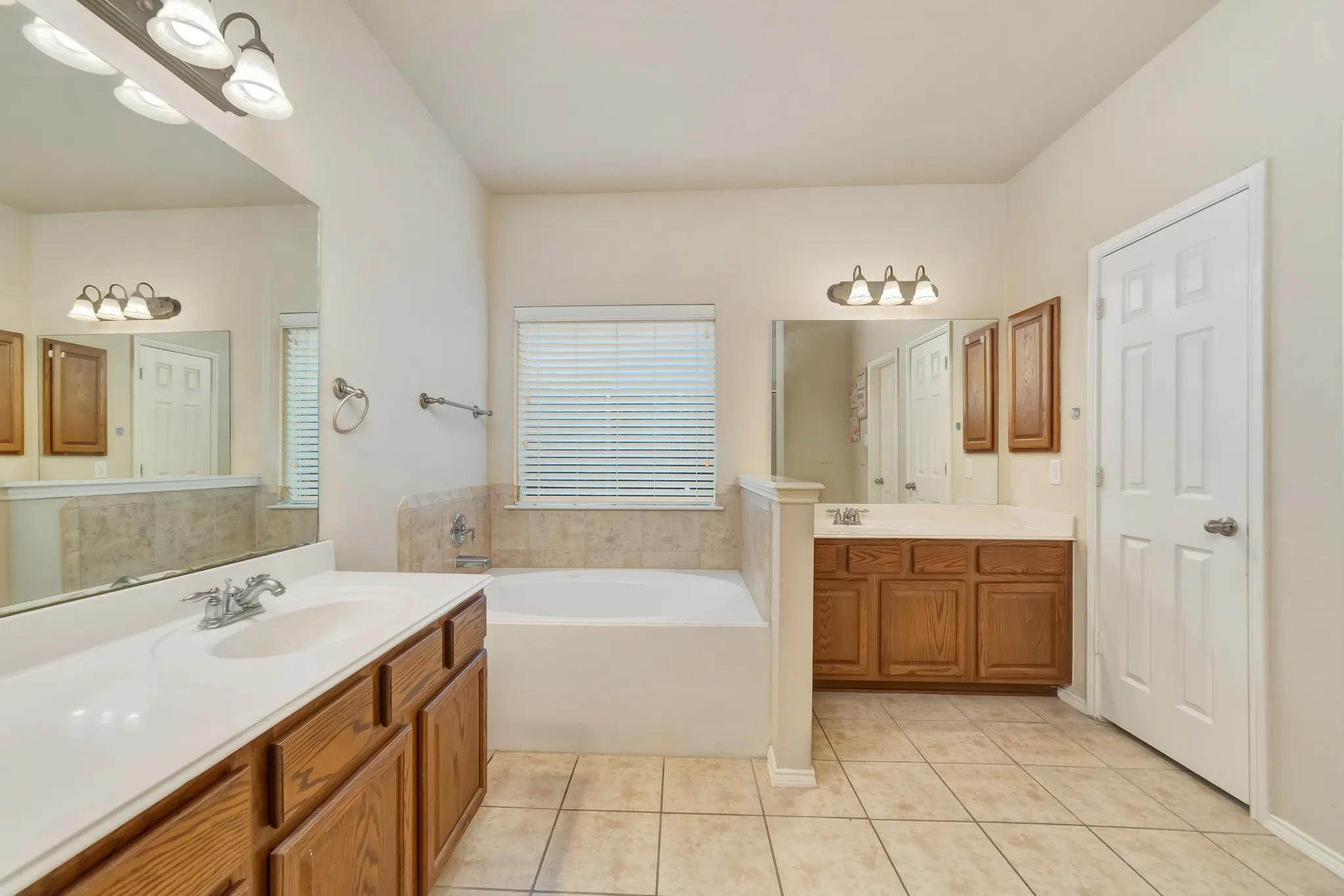 Bathroom featuring dual vanities, a built-in garden tub, tile flooring, and neutral wall tones