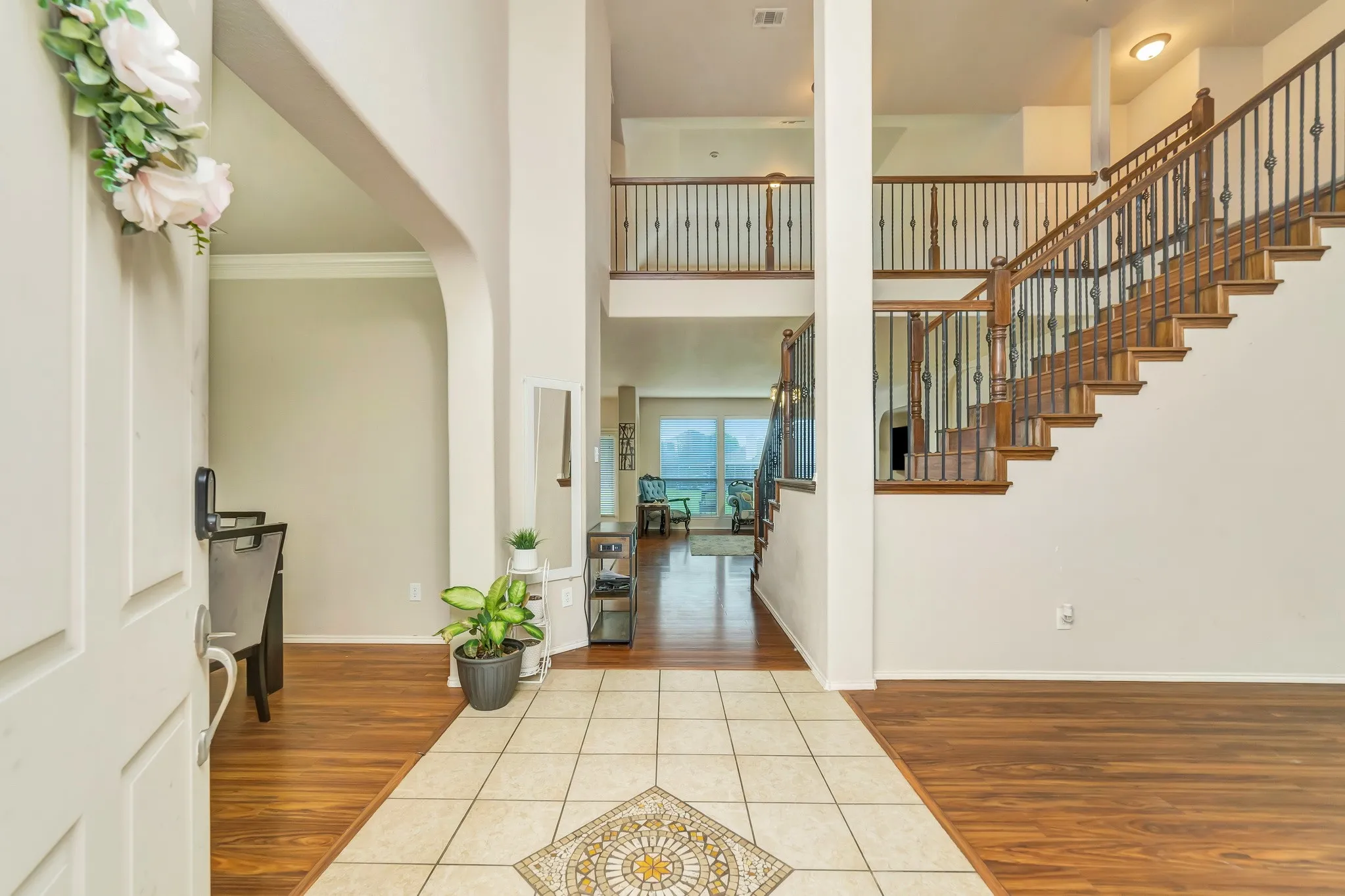 Two-story foyer featuring wood-finish flooring, a ceramic tile entry with a decorative inlay, and a grand staircase with wood treads and wrought iron balusters