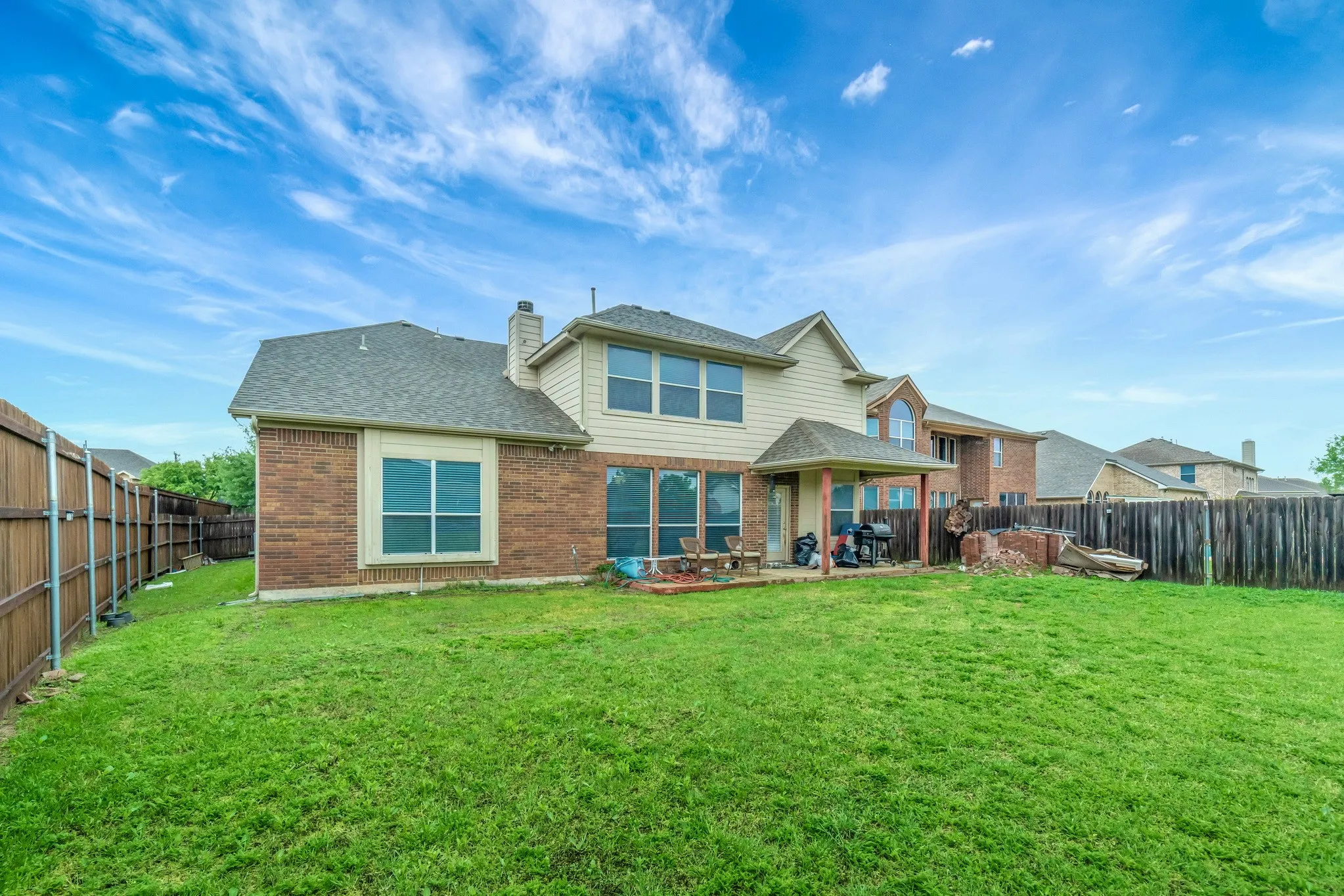 Spacious backyard featuring a covered patio, extensive lawn, full privacy fencing, and a two-story exterior with brick and siding finishes