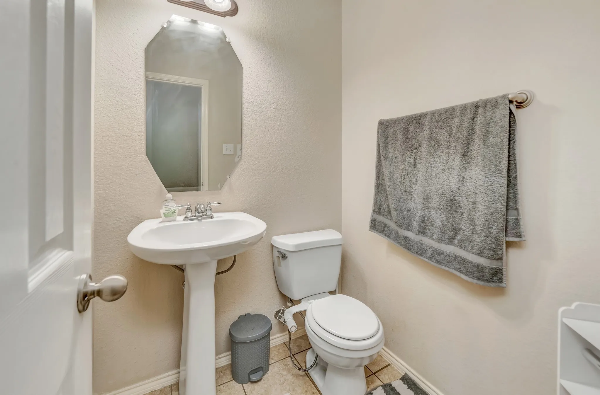 Pedestal sink featuring a chrome faucet, illuminated by an overhead light fixture