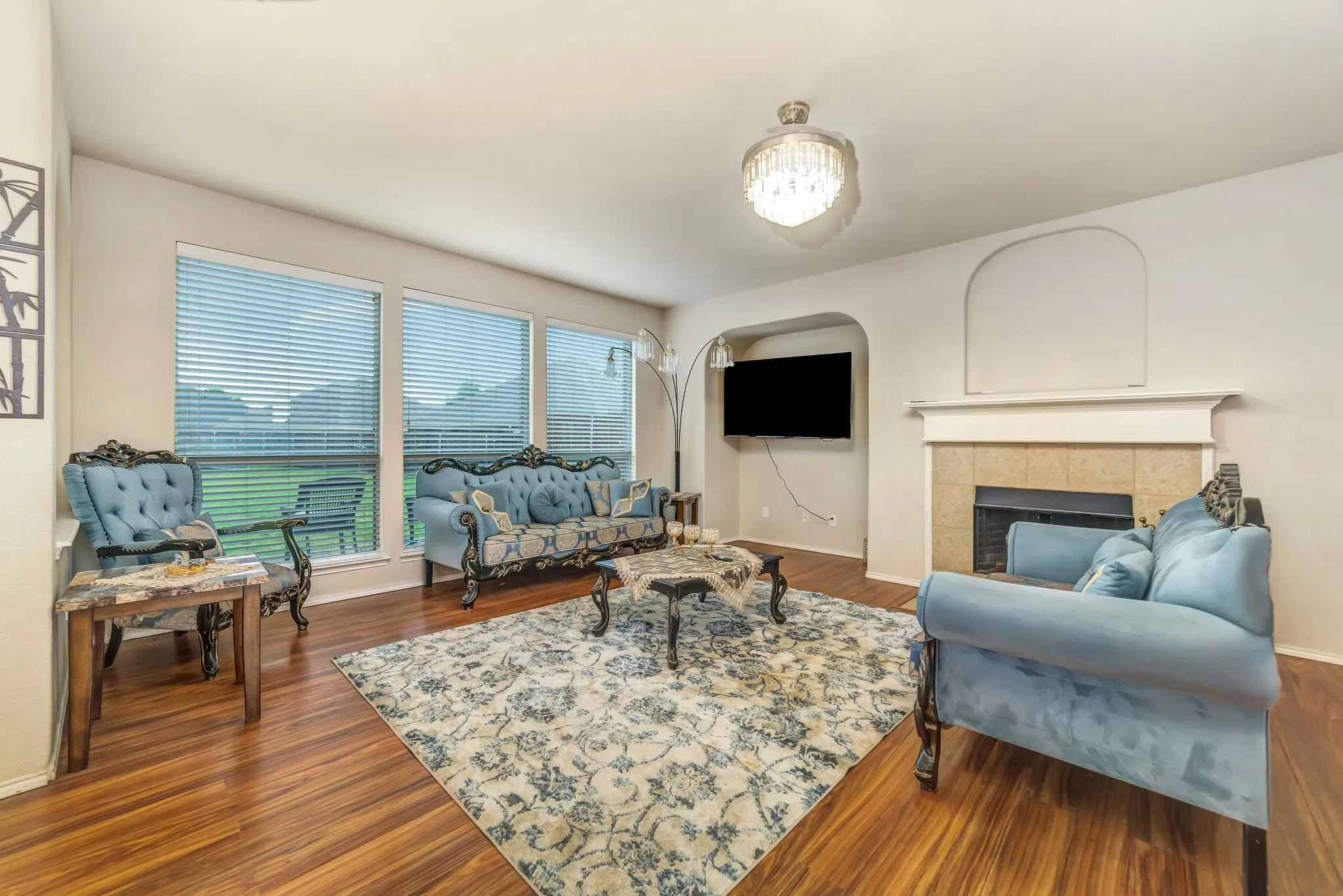 Living area featuring wood-finish flooring, a decorative chandelier, and multiple windows with horizontal blinds