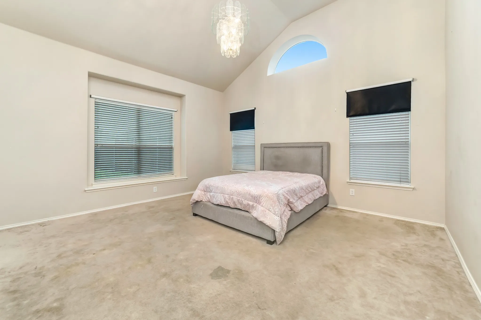Room featuring a vaulted ceiling with an elegant chandelier, beige carpeting, and multiple windows