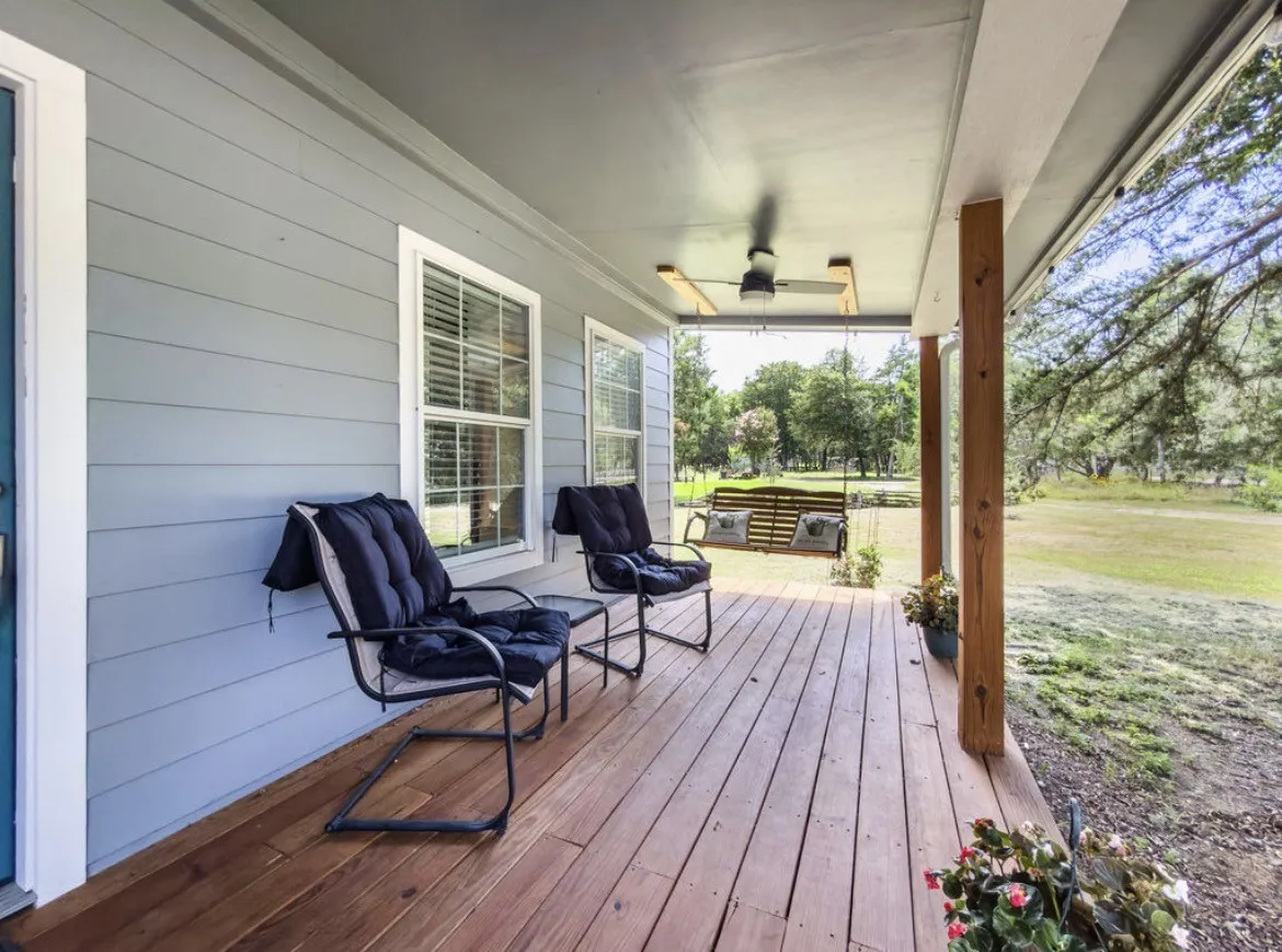 Covered wood-finish porch featuring a ceiling fan with integrated lighting, wood support columns, and light gray horizontal siding